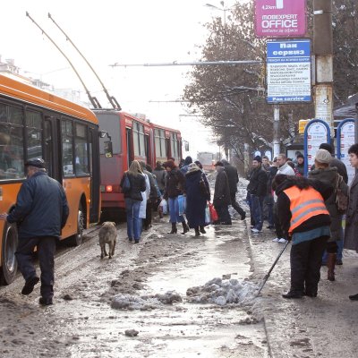 Служителка премества снега от тротоара на спирката на  Орлов мост  на платното
