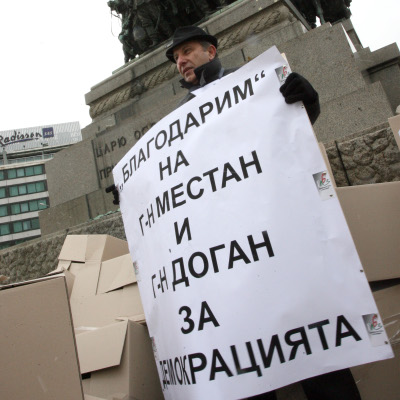 Протестиращ носи плакат, който обяснява срещу какво недоволства
