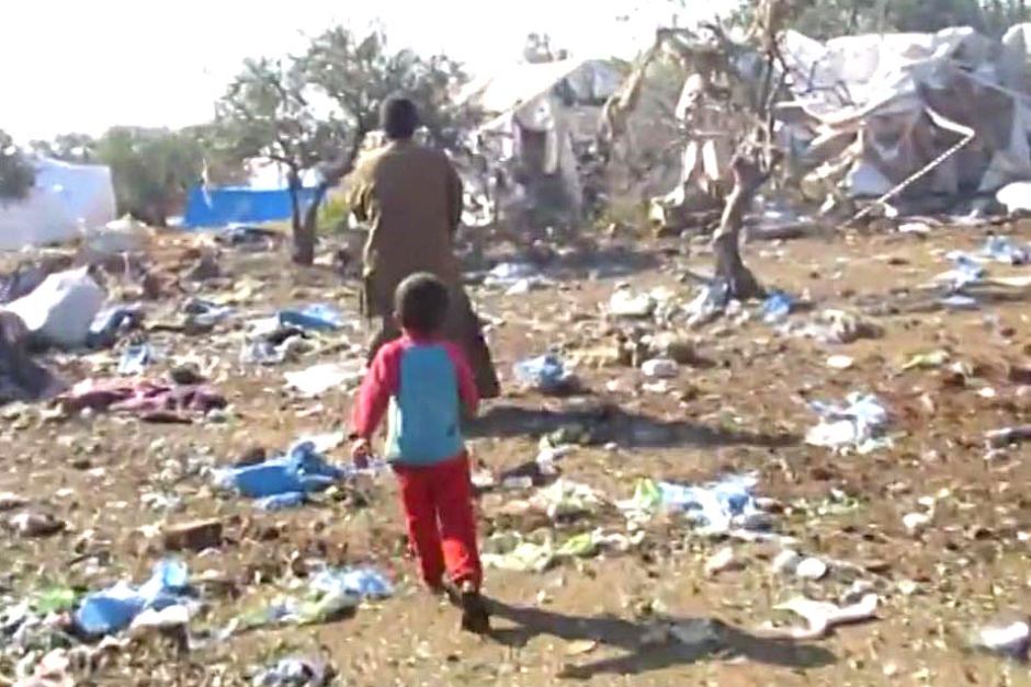 Мъж и дете от лагера вървят сред отломки и унищожени палатки