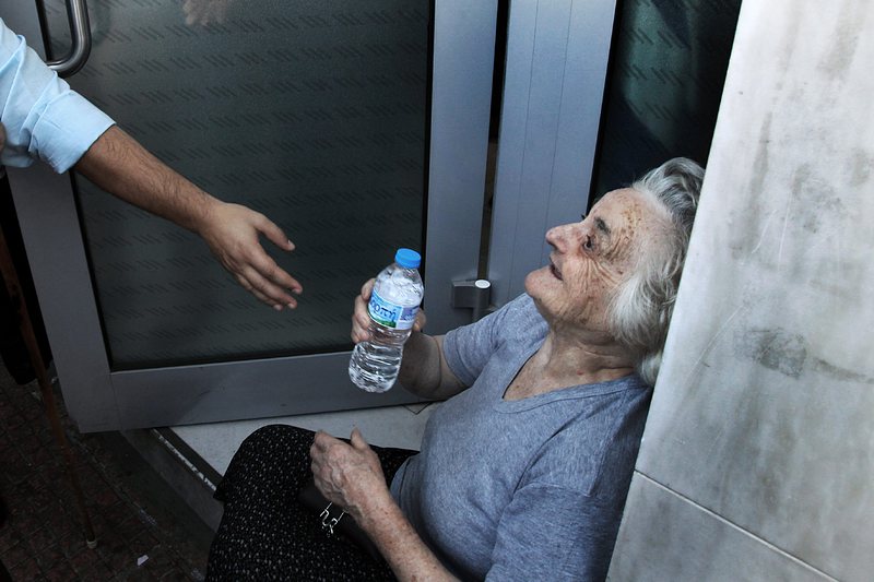 Възрастна жена получава вода на опашка пред банков клон в Гърция
