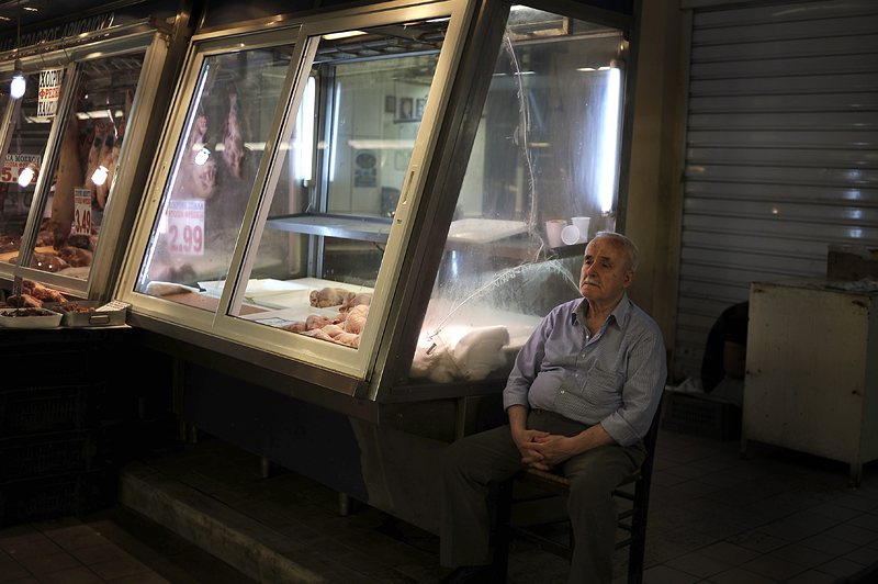 Мъж седи до магазин на месния пазар в Атина, Гърция