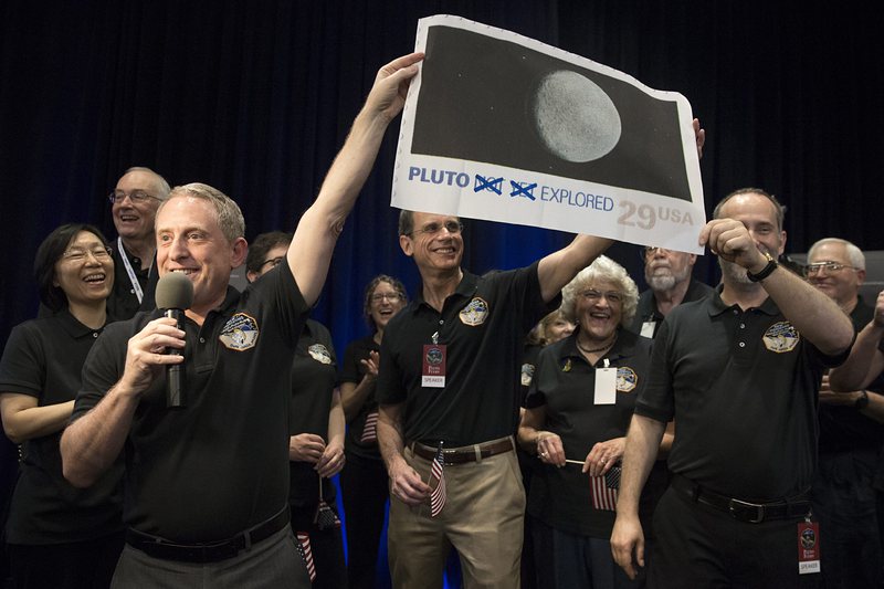 Изследователят на проекта ”Нови хоризонти” Алън Стърн (вляво) държи уголемен размер на 29-центова марка, изобразяваща планетата