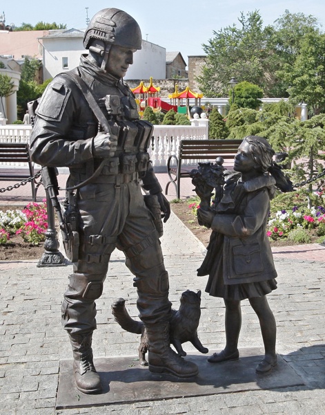 Войникът гледа закрилнически момиченце, котка се търка в краката му