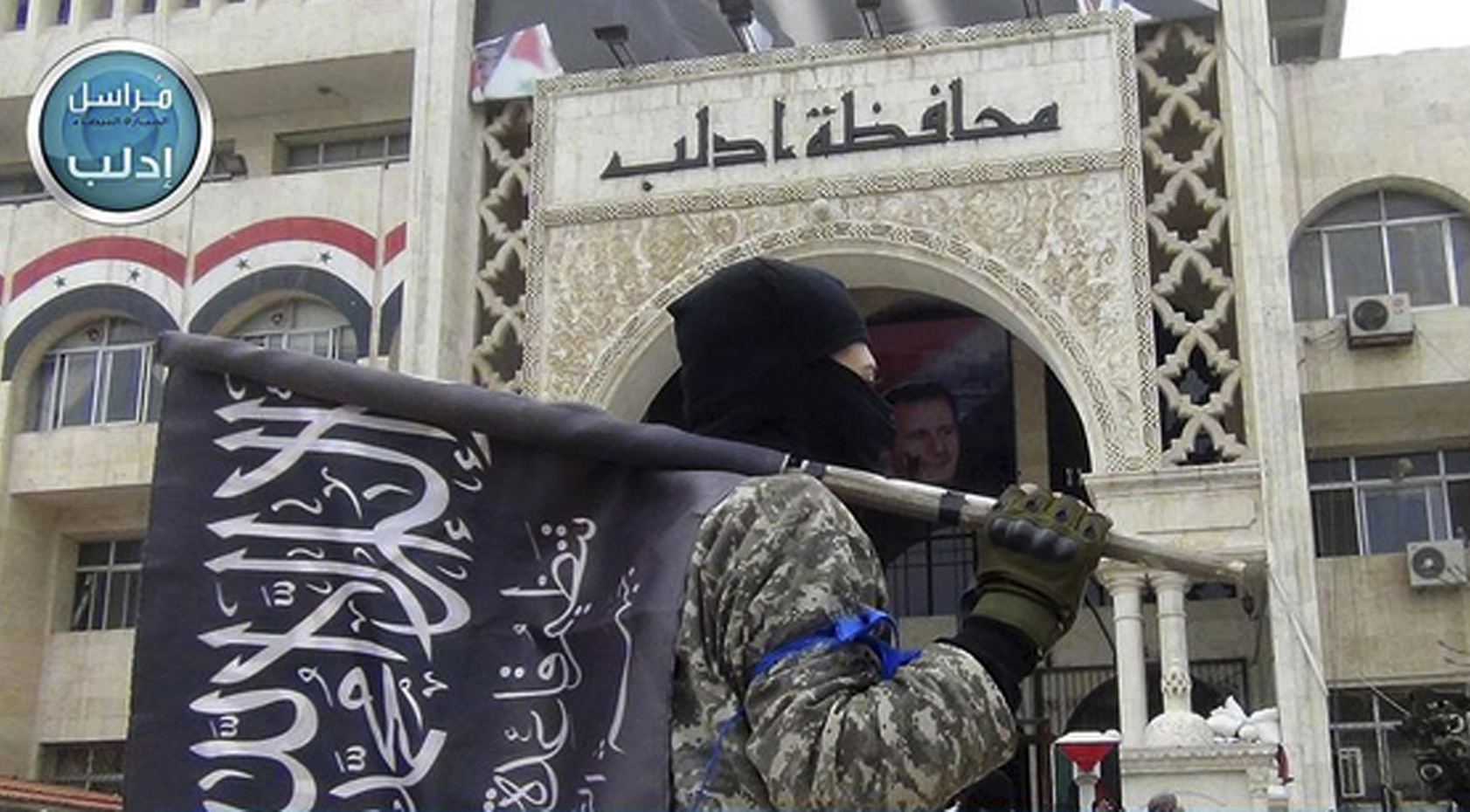 Снимка на Фронта Ан Нусра (свързан с Ал Кайда). Боец държи знамето на Фронта пред правителствена сграда в Идлиб, Северна Сирия
