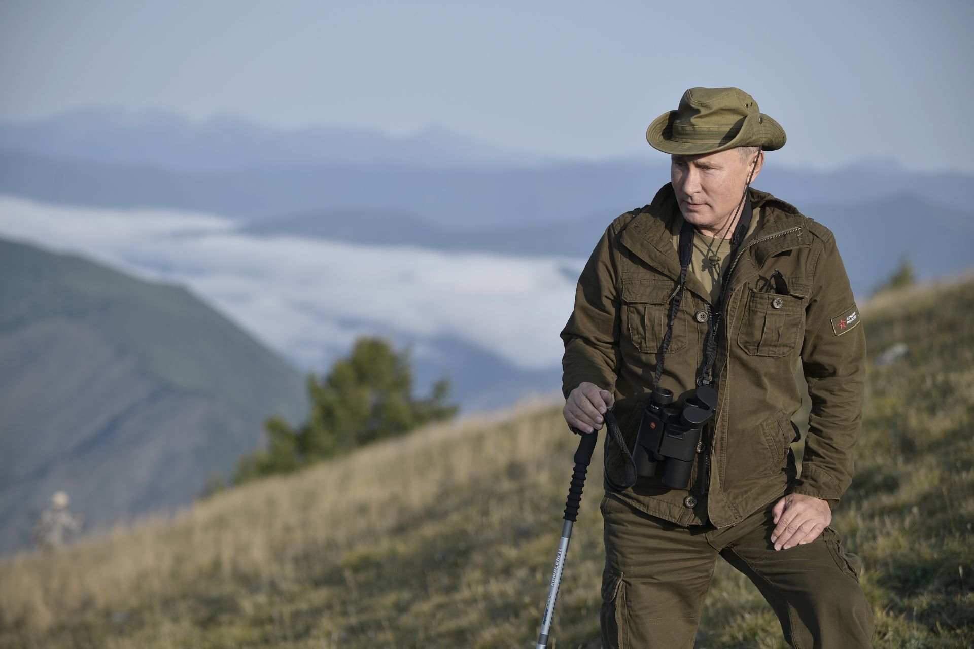65-годишният Путин в дрехи цвят каки и шапка да носи бинокъл и туристическа щека и да се разхожда из гористите планини
