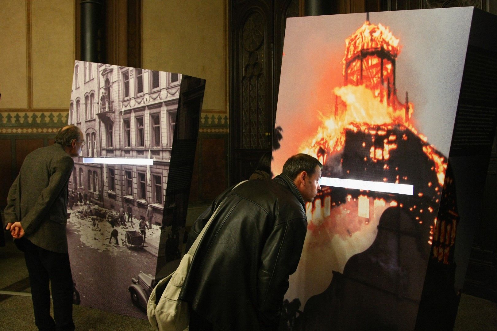 Посетители в германски музей гледат снимки на горяща синагога и други архивни кадри