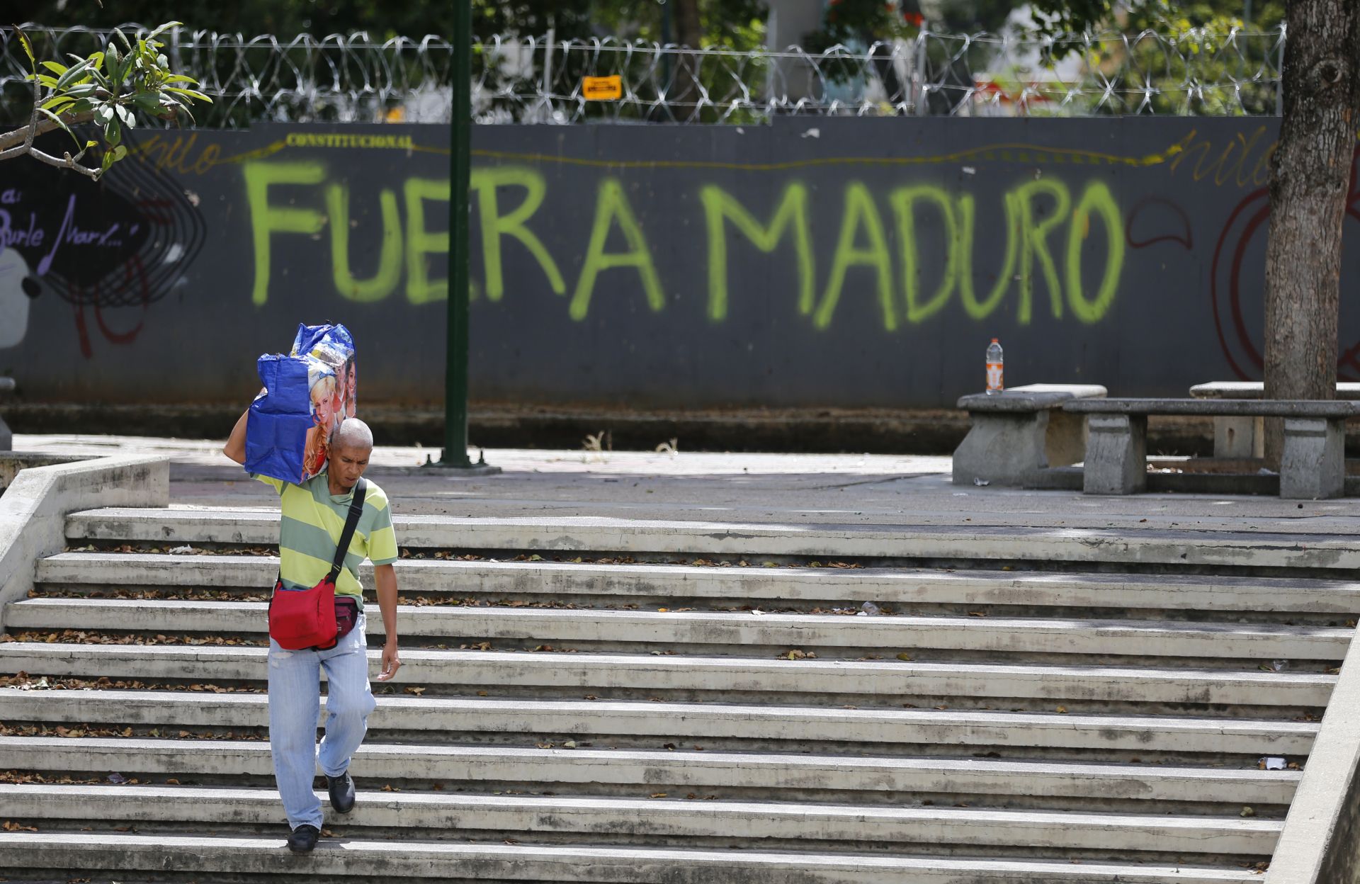 Графит в Каракас, на който пише Един мъж минава покрай графити на стената на свободно място, което пише на испански: "Махай се Мадуро"