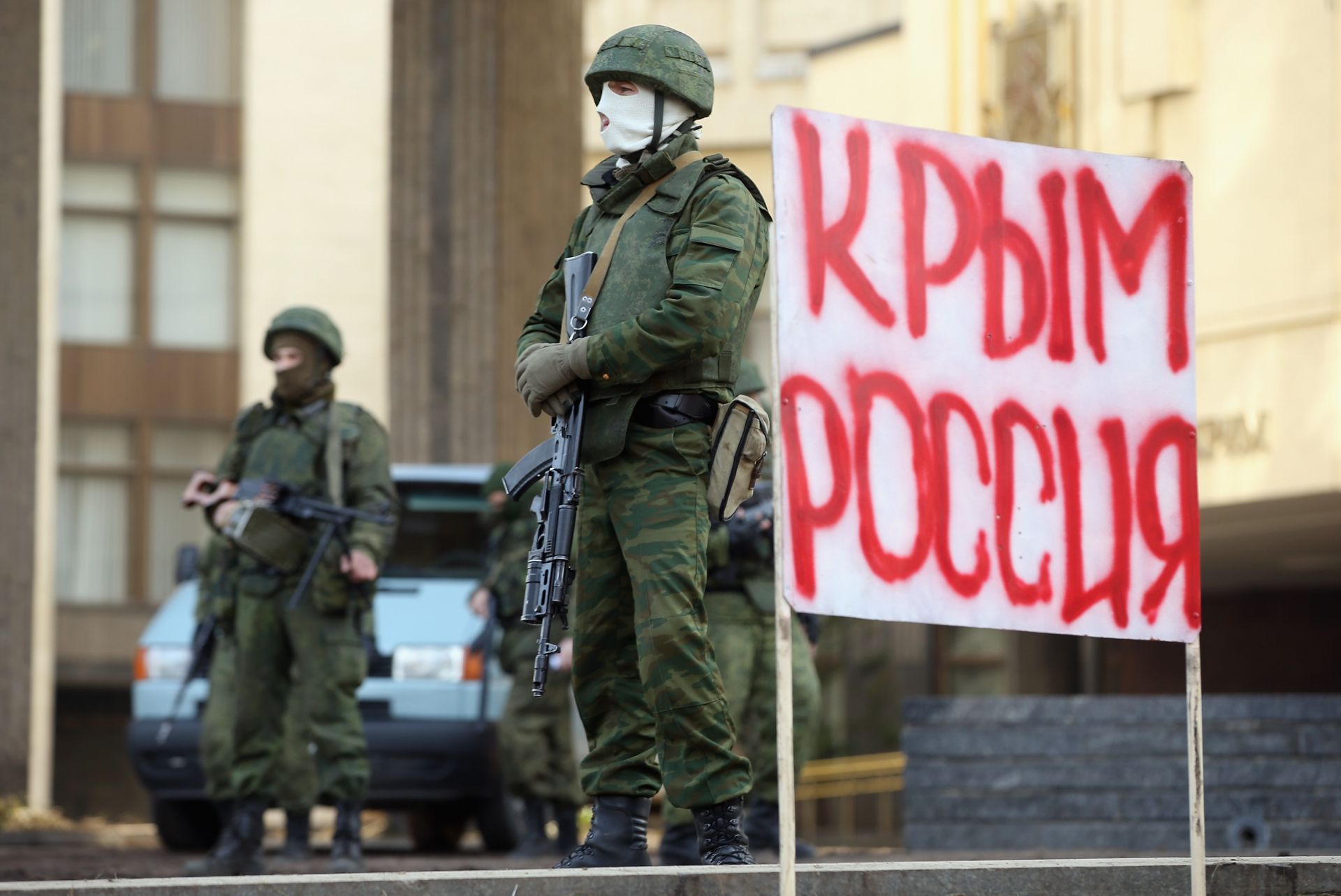 1 март 2014 г.: Тежко въоръжени войници без идентифицирани знаци охраняващи сградата на Кримския парламент до знак, който гласи: "Кримска Русия"