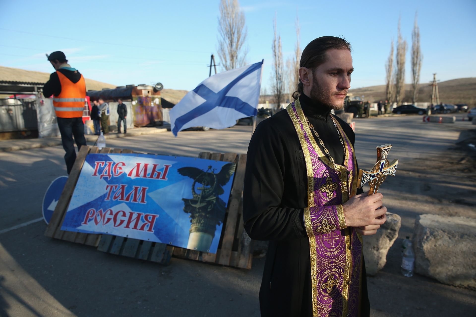 Духовник носи кръст след като се моли за мир и позволява на проруски бойци да целуват икони на контролно-пропускателен пункт, където на 3 март 2014 г. има надпис „Където сме, има Русия“,  близо до Белбек