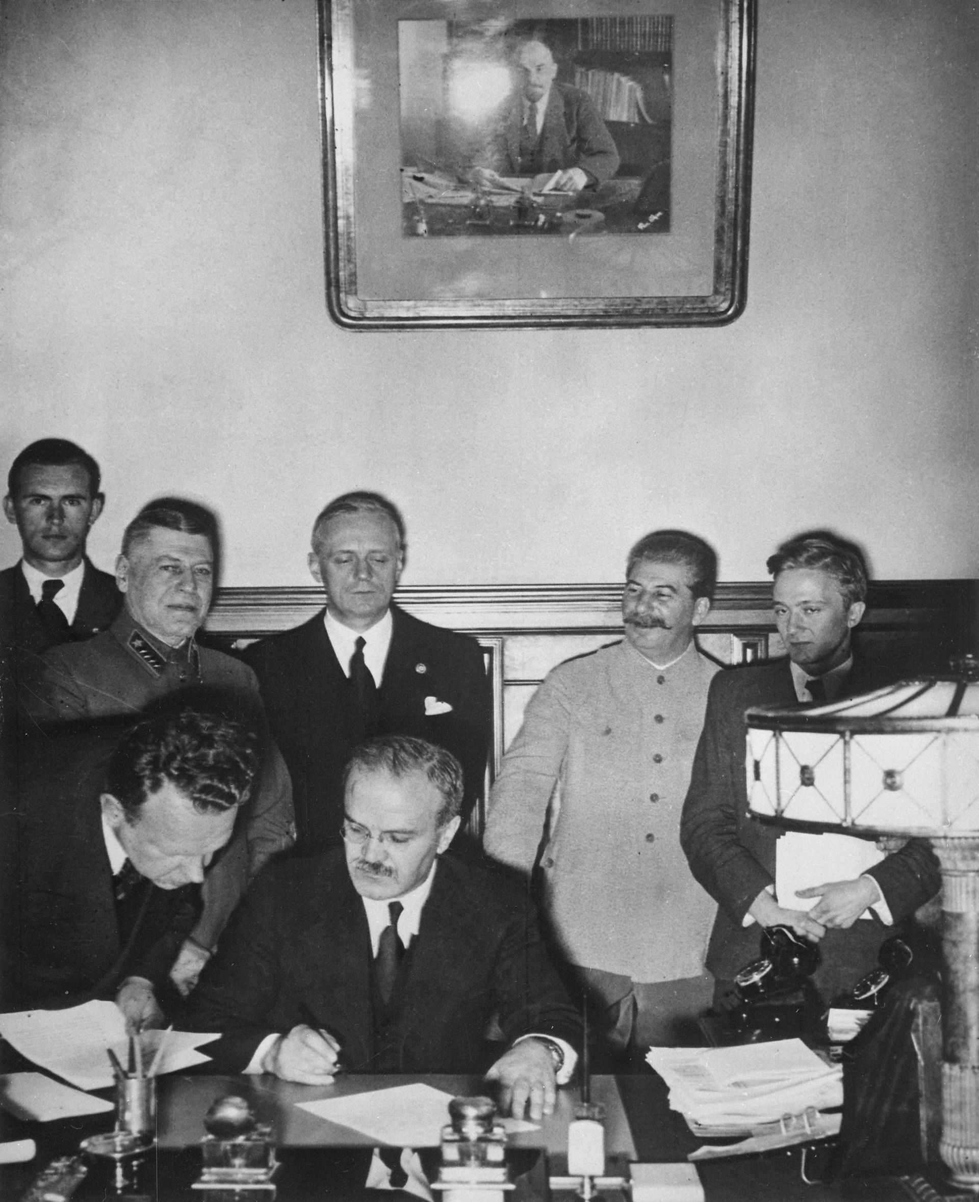Вячеслав Молотов подписва пакта за ненападение между Германия и СССР. На заден план са Йоахим фон Рибентроп и Йосиф Сталин