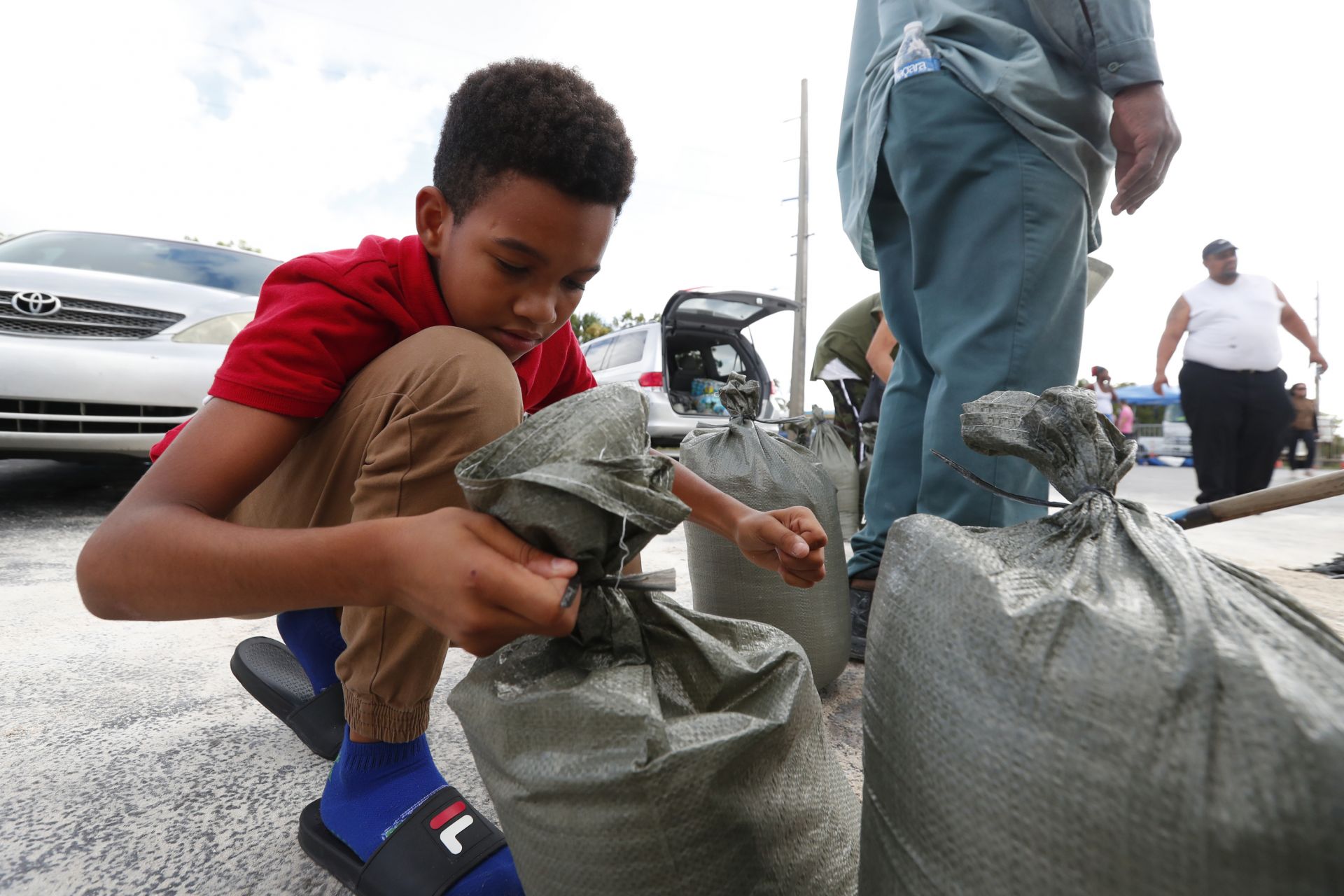 Исая Ели, на 11 години, завързва торби с пясък, тъй като семейството му ги запълва при подготовката за урагана Дориан