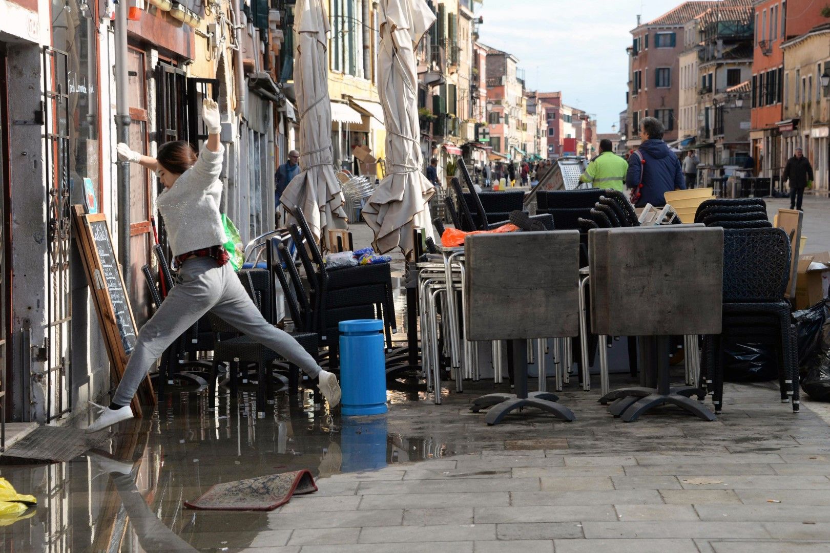 Жена прескача локва, останала от високата вода, докато почиства след наводнението във Венеция