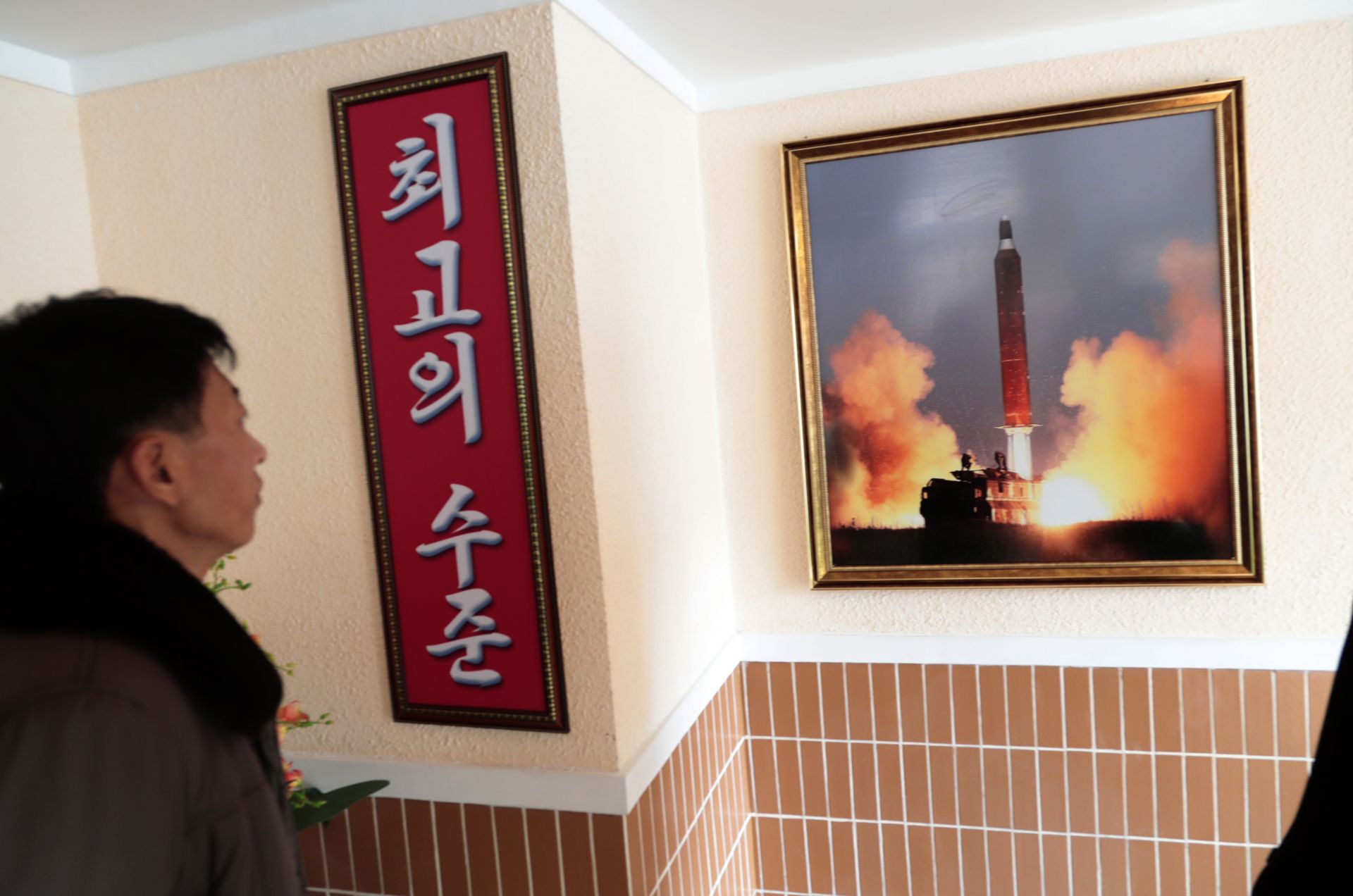 В тази снимка от 26 ноември 2019 г. мъж гледа снимка на изстрелването на ракета, окачена на стената на работническо общежитие в Пхенян