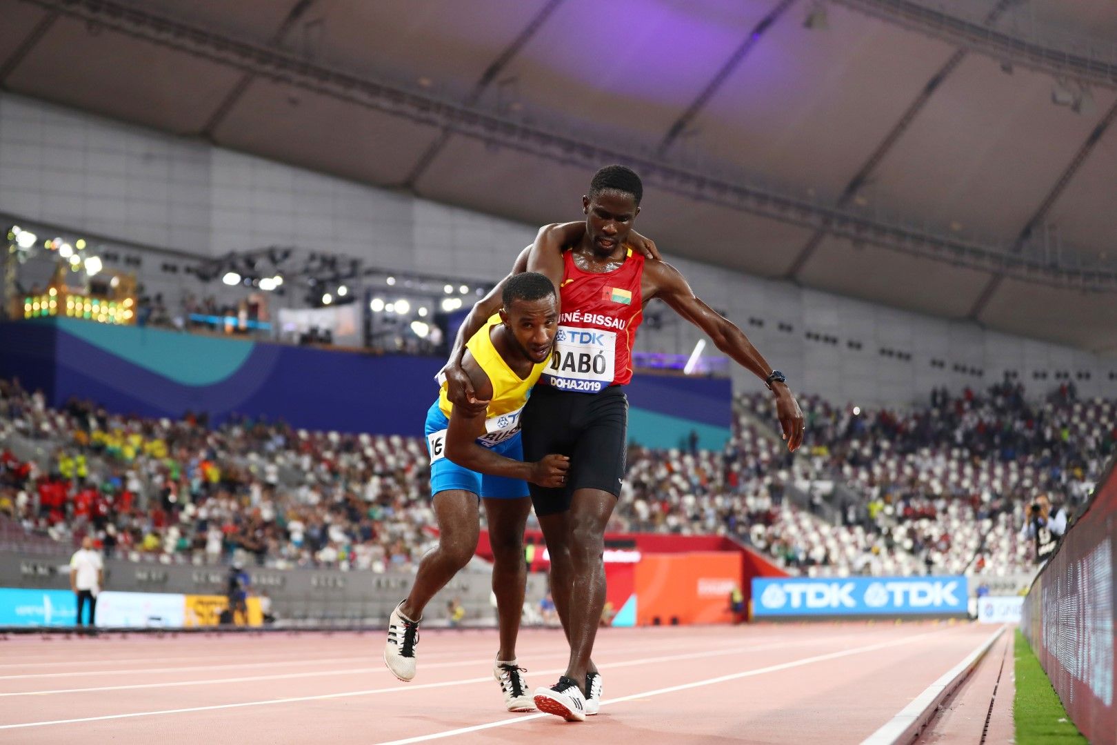 Световно първенство по лека атлетика, Доха. Браима Дабо от Гвинея Бисау помага на Джонатан Бъзби от Аруба да финишира по време на бягането на 5000 м. Огромните жеги и влажност съсипаха състезателите.