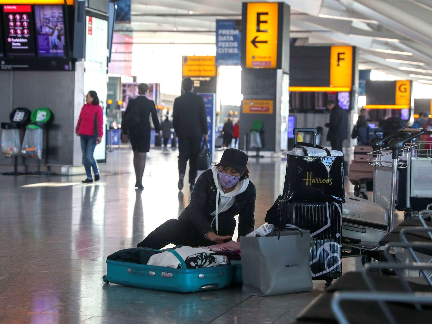 Жена, носеща маска за лице, събира куфара си в зоната на излитане на Терминал 5, на лондонското летище Хийтроу