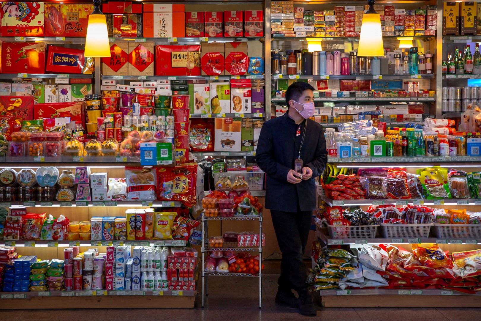 Магазин с пакетирани храни и собственикът му, който чака клиенти на гарата в Пекин