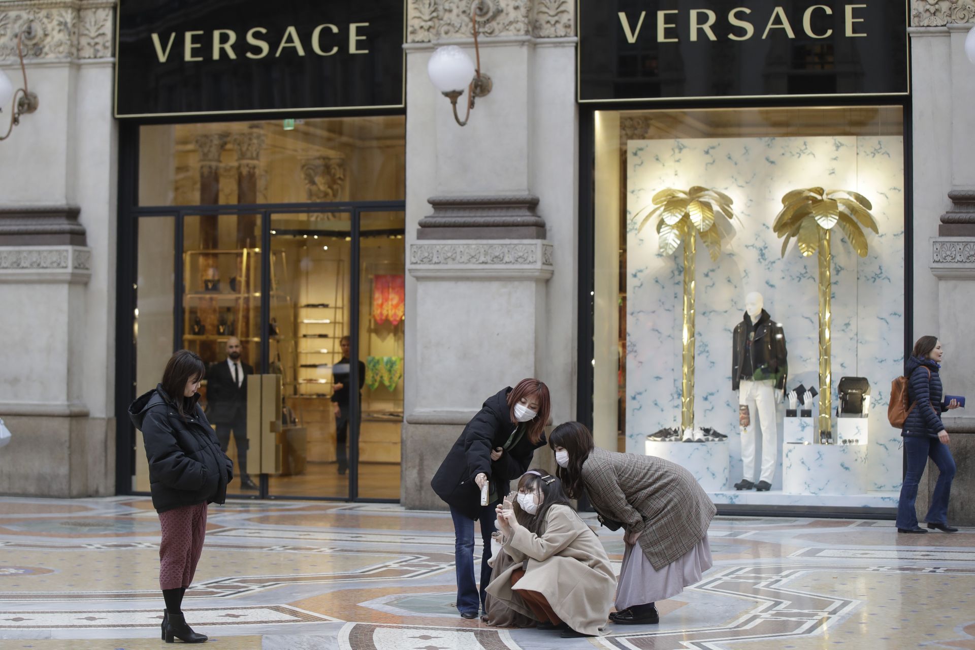 Туристите, облечени с маски за лице, позират за селфи пред витрина на Versace в центъра на Милано