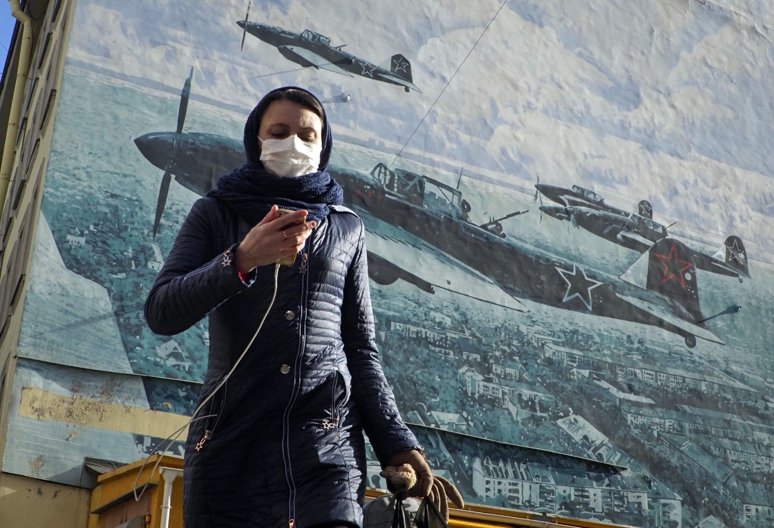 Рускиня се разхожда с маска в Санкт Петербург на фона на плакат, изобразяващ самолети от Втората световна война