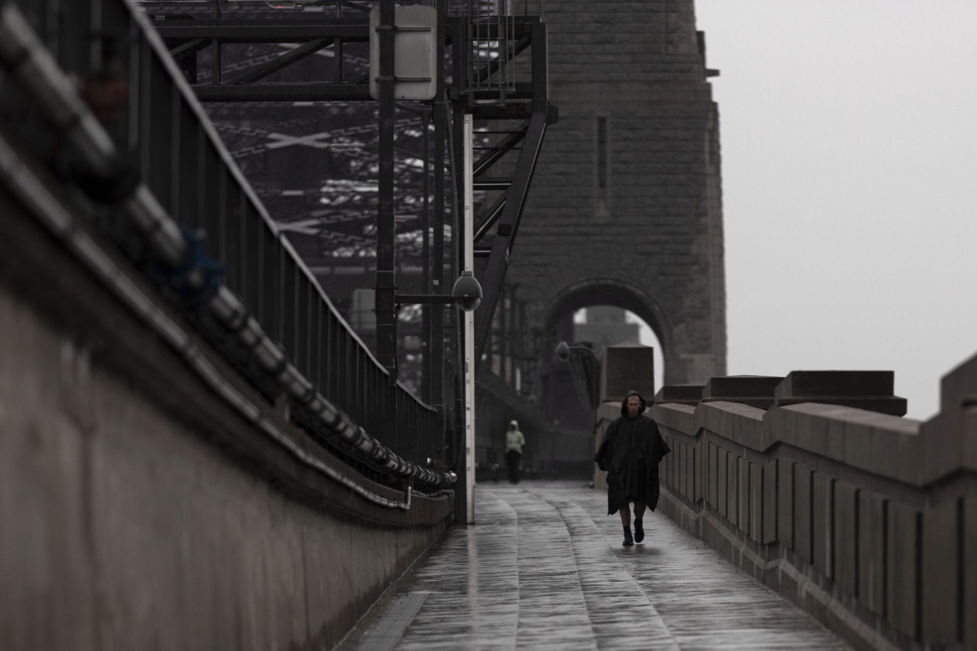  Мъж минава през моста на пристанището в Сидни под силен дъжд по време на частичното блокиране на града