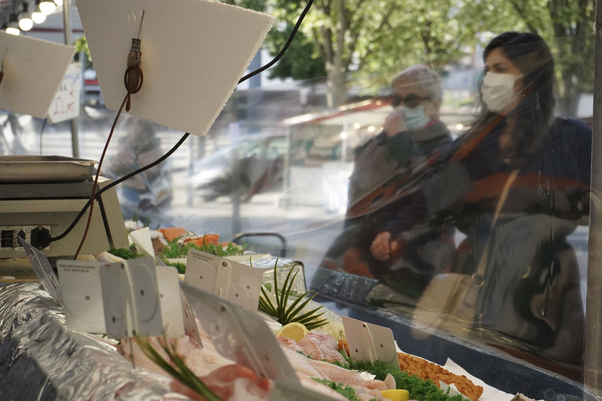 Клиенти стоят пред рибен щанд зад защитна пластмасва бариера 