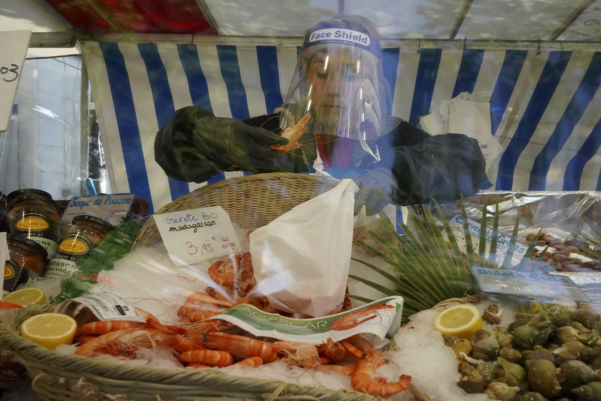 Рибарник носи щит за лице, докато работи на парижки пазар на хранителни продукти на открито