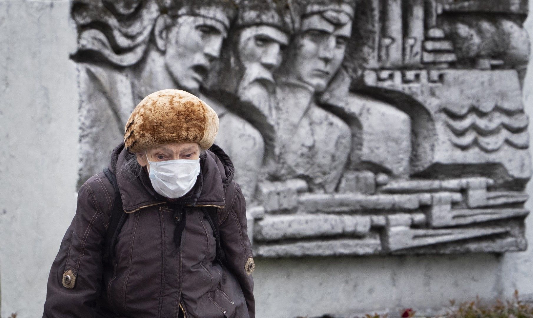 Възрастна жена с маска минава край монумент от съветската ера в Санкт Петербург