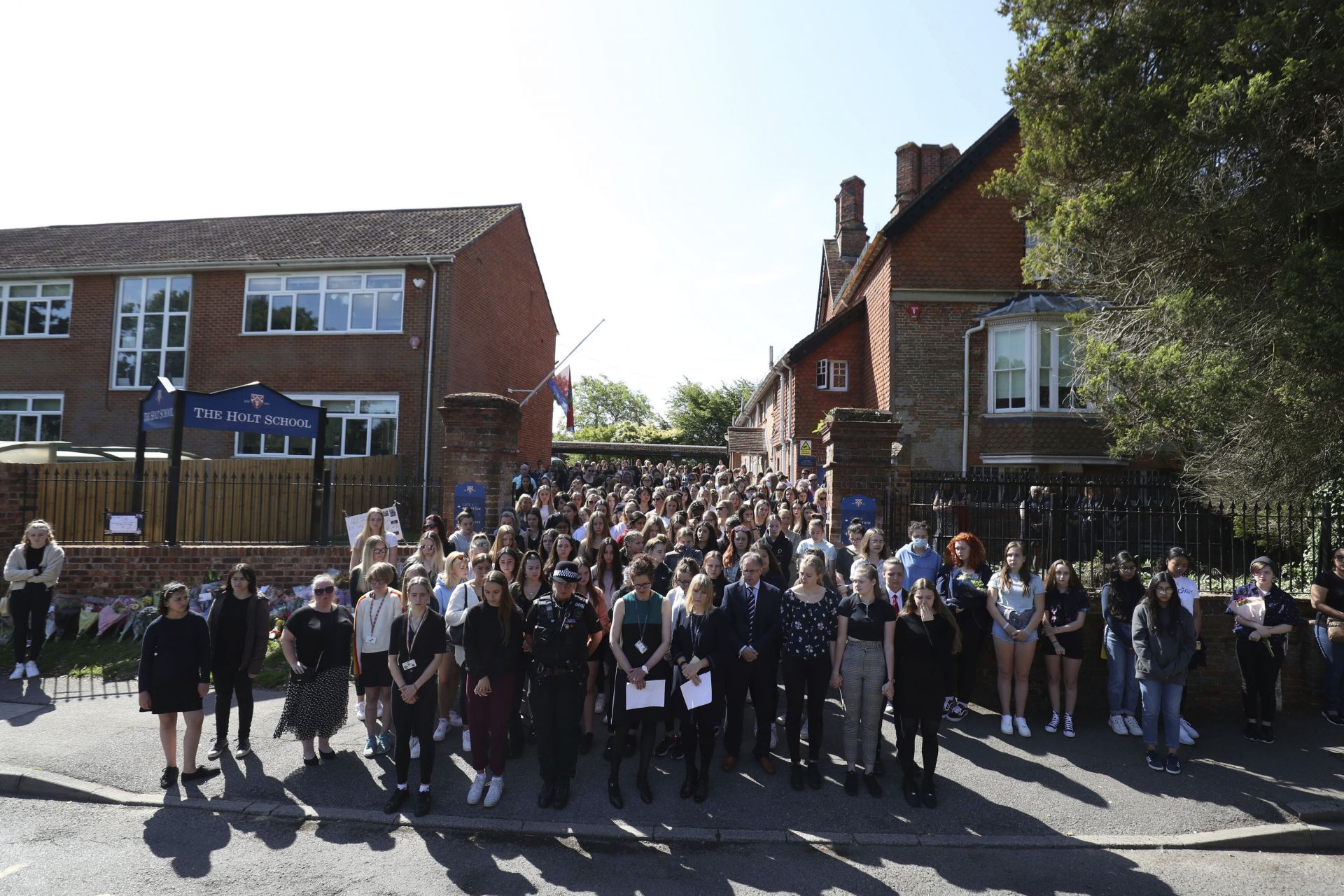 Над 100 ученици, някои от които се държаха за ръце, се събраха пред входа на училището, за да отдадат минута мълчания в памет на любимия си учител