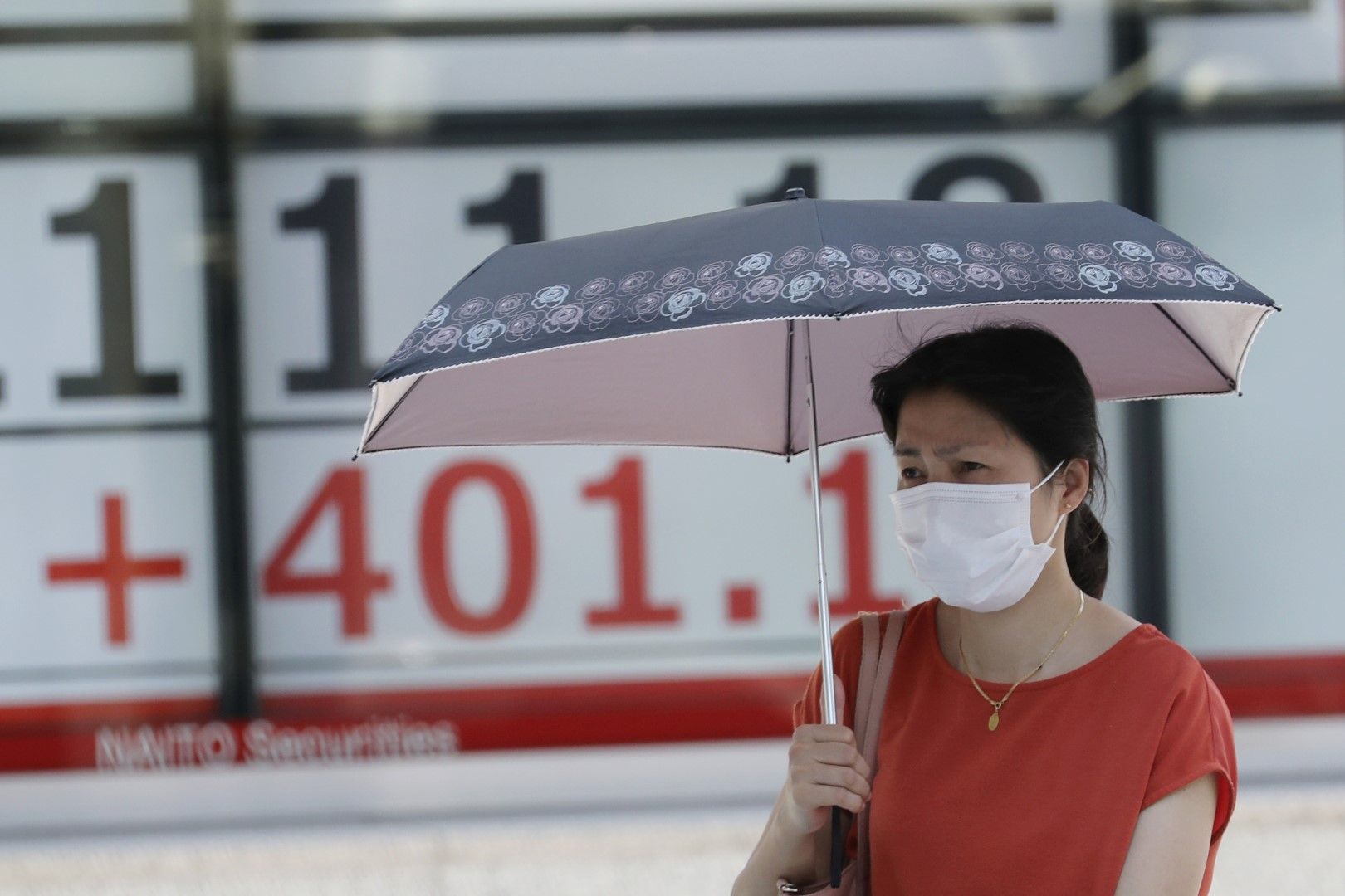 Жена с маска на лицето минава покрай електронно табло в Токио, което показва движението на индекса Никей, 3 август 