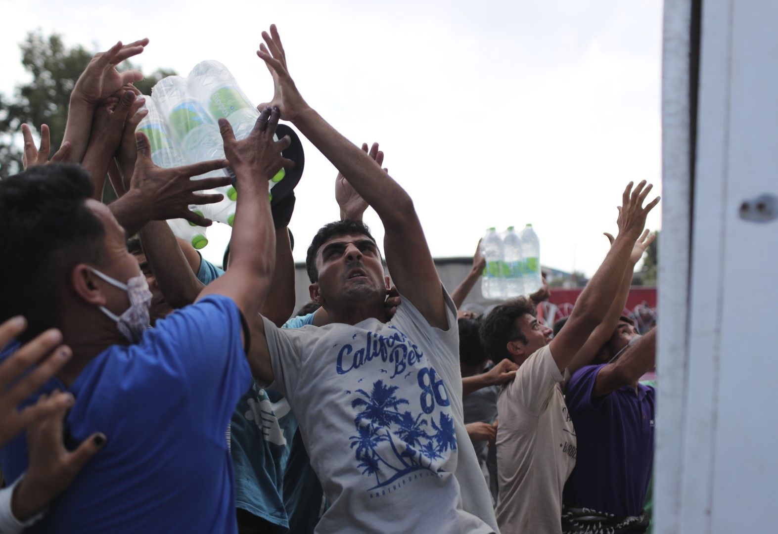 Мигранти се опитват да хванат бутилки минерална вода, осигурена от властите на остров Лесбос