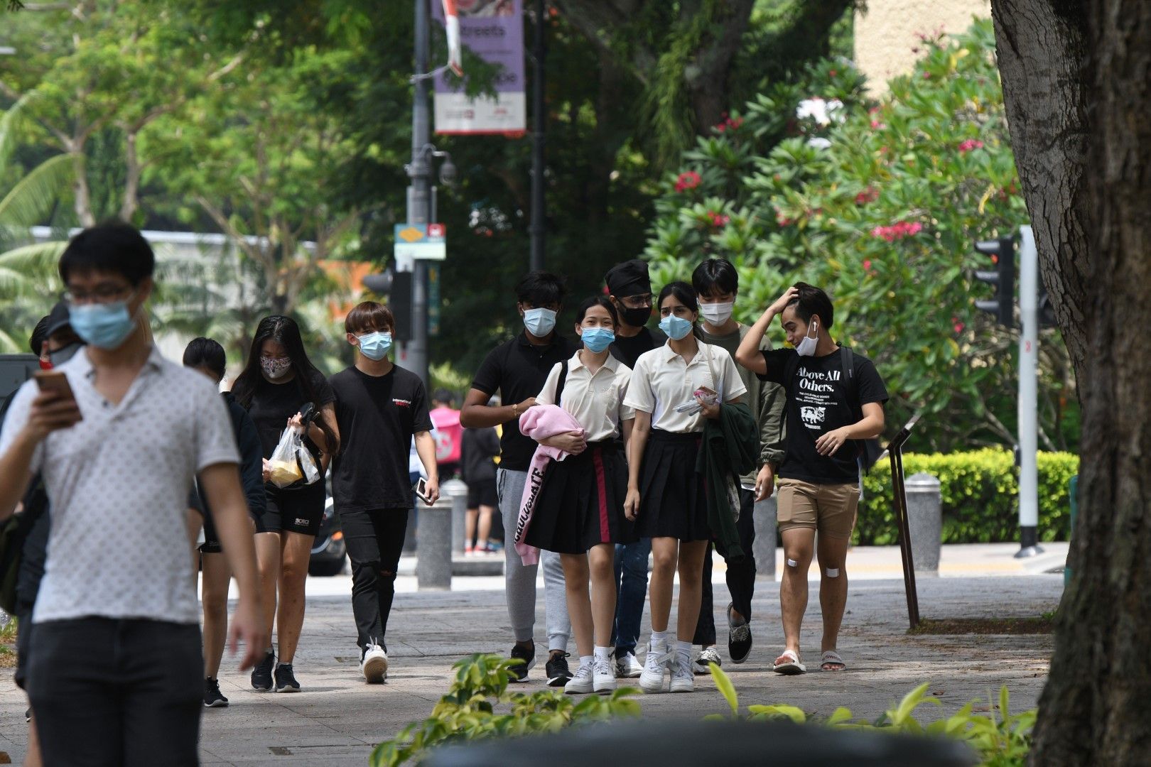 Млади хора с предпазни маски се разхождат по централна улица в Сингапур. Към юни тази година населението на страната наброява 5,69 милиона души