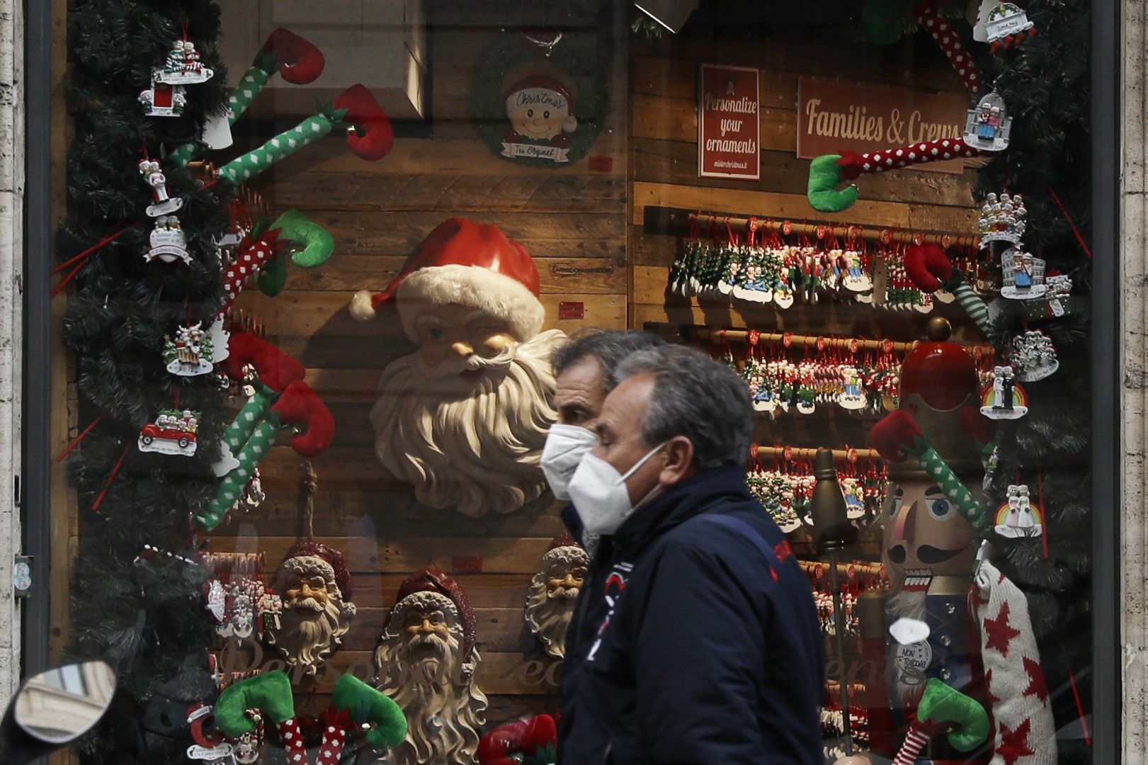 Мъже с предпазни маски минават покрай коледно украсена витрина на магазин в Рим