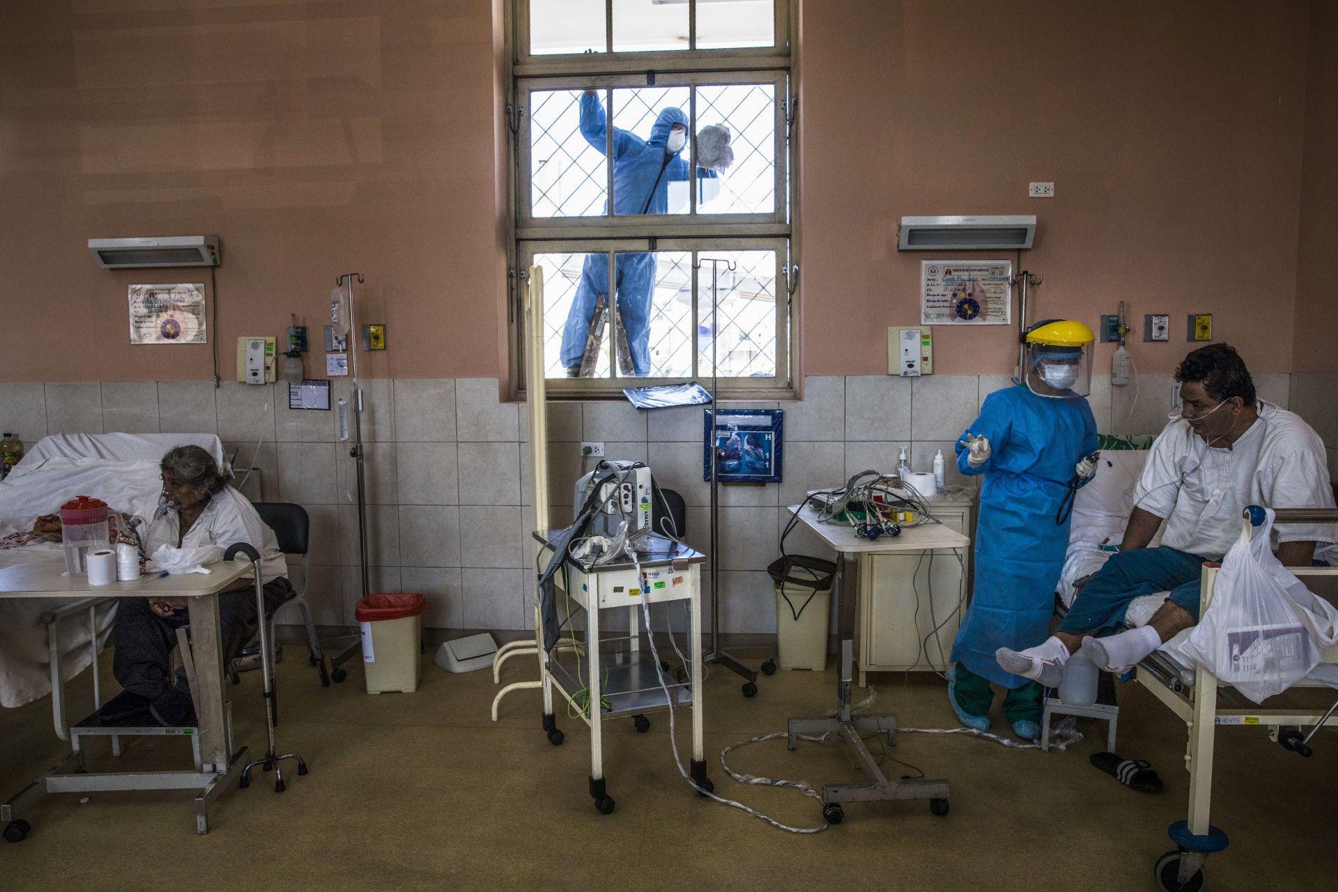 Работник, носещ защитно оборудване, почиства прозореца, докато медицинска сестра се грижи за пациент в интензивното отделение за хора, заразени с коронавирус в болница в Лима, Перу. (17 април 2020 г.)