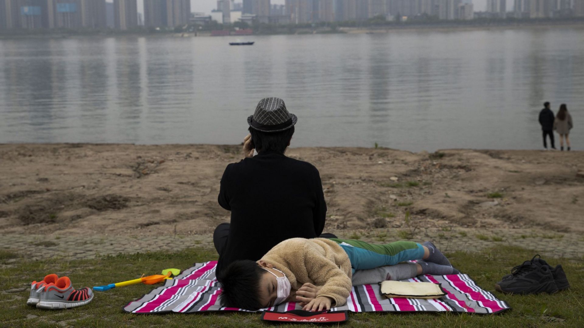  Дете с маска против ковид почива на брега на река Яндзъ в Ухан, в централната китайска провинция Хубей (16 април 2020 г.) 