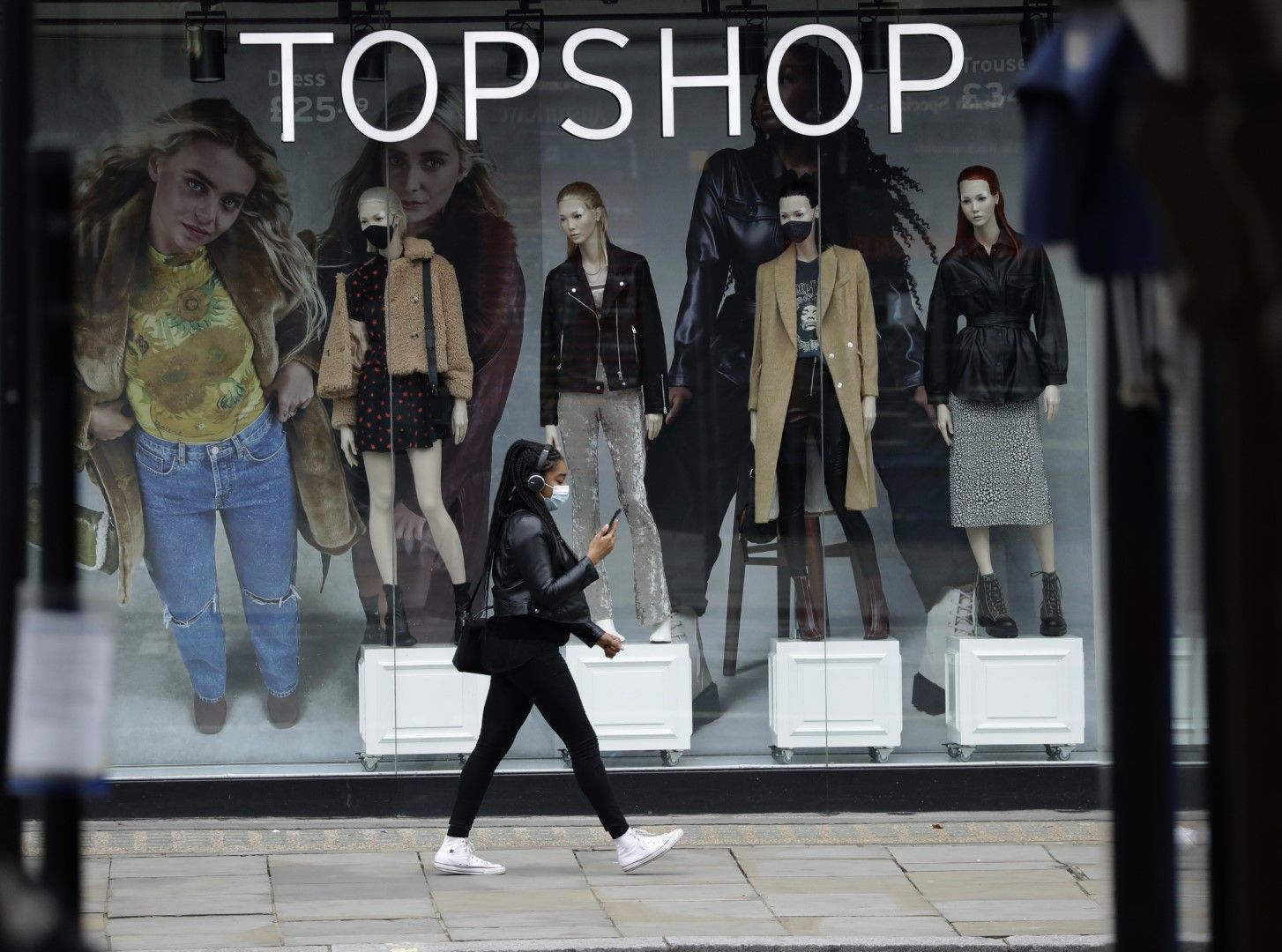 Жена с маска за лице минава покрай манекени с маски на витрина на вренно затворен магазин на веригата дамски дрехи Topshop в Лондон, 20 ноември 2020 г.