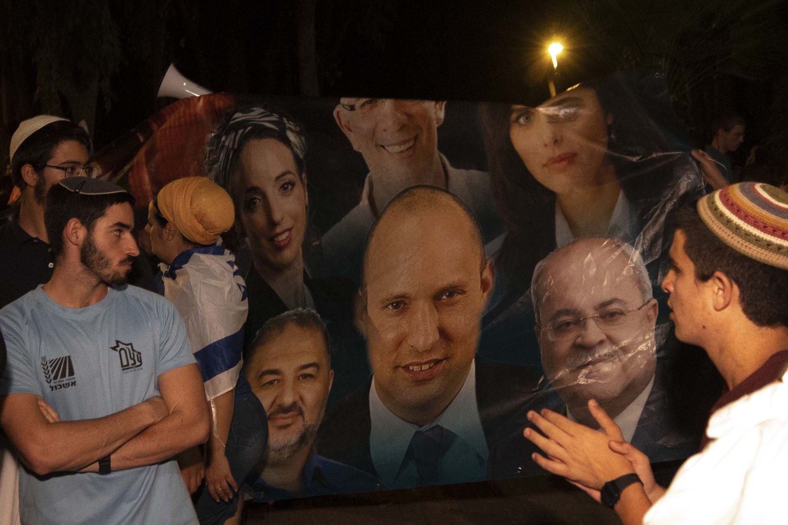 Израелски десни активисти скандират лозунги и държат плакати, показващи Нафтали Бенет, лидер на партия Ямина (в средата) и арабските политици Ахмад Тиби (вдясно) и Мансур Абас (вляво) по време на демонстрация в Тел Авив срещу формиране на ново правителств
