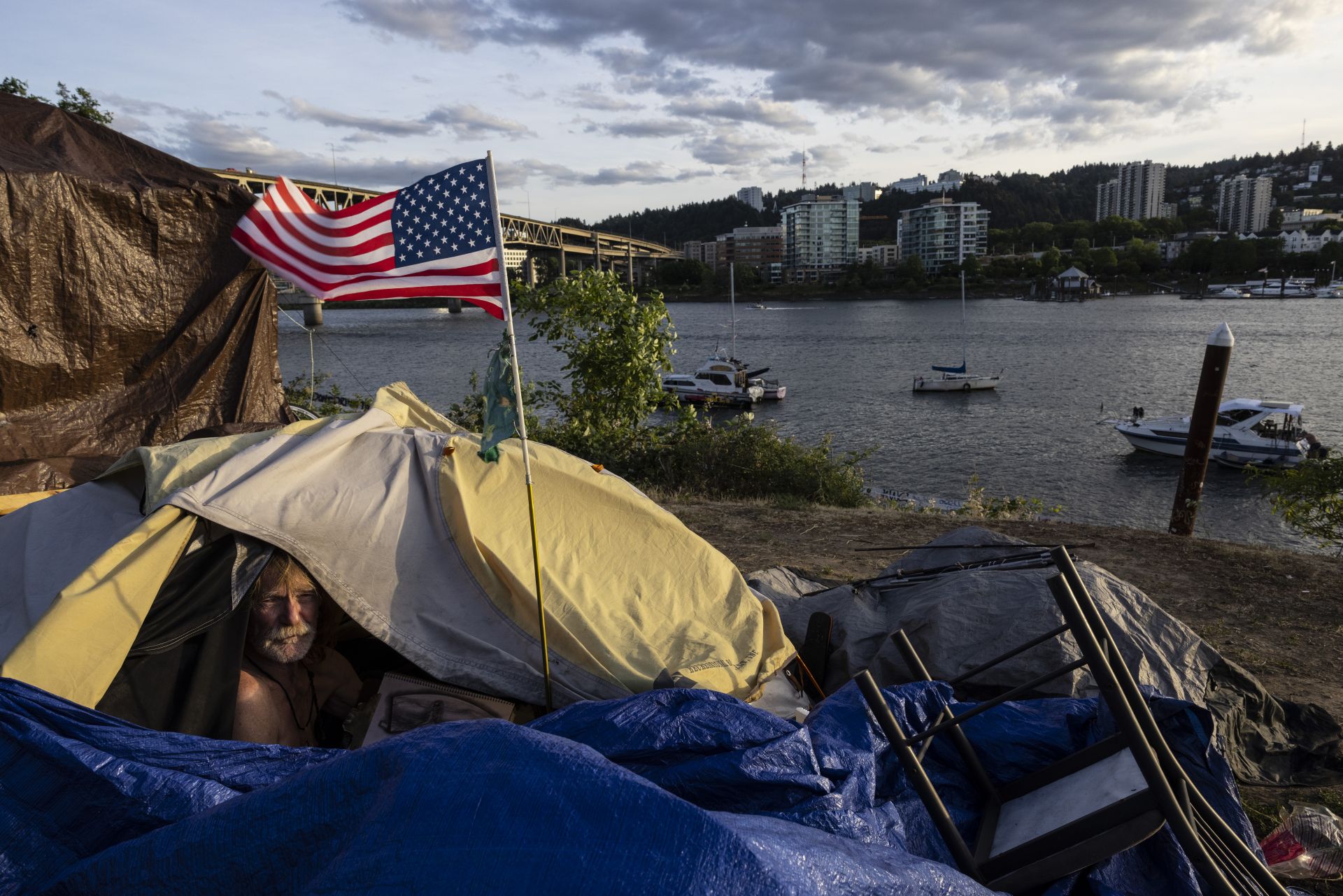 10 юни 2021 г. - Бездомникът Франк стои в палатката си с изглед към реката в Портланд, Орегон. Протестите след убийството на Джордж Флойд, нарастването на смъртта от въоръжено насилие и все повечето бездомници предизвикват въпроса, дали най-големият град в Орегон може да се възстанови.