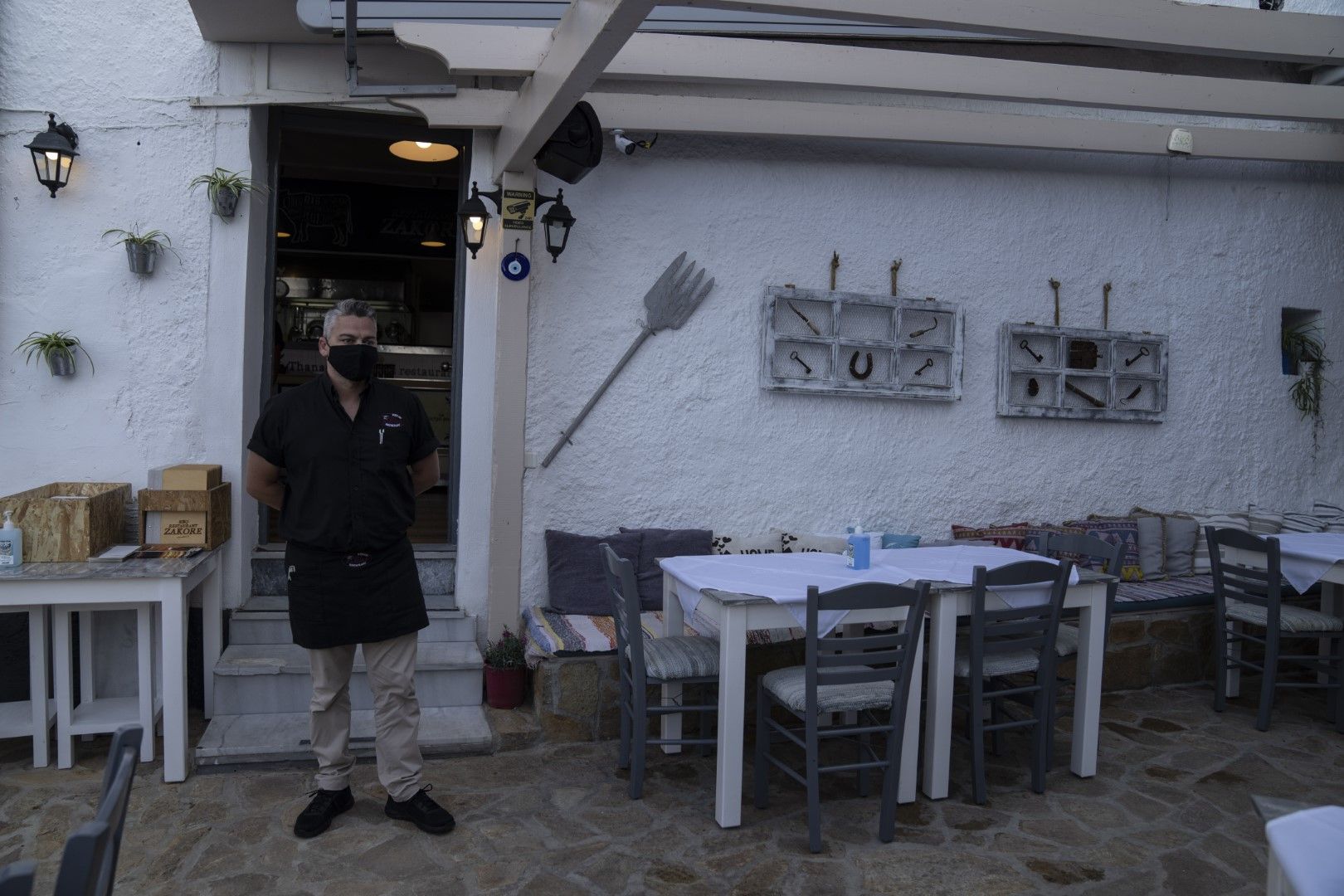 Танасис Сафис със защитна маска за лице стои пред ресторанта, който управлява, на пристанището Кокари на източния Егейски остров Самос, 8 юни 2021 г. Заведенията в Гърция ще работят само със седящи клиенти и в съответствие с определените правила за капаци
