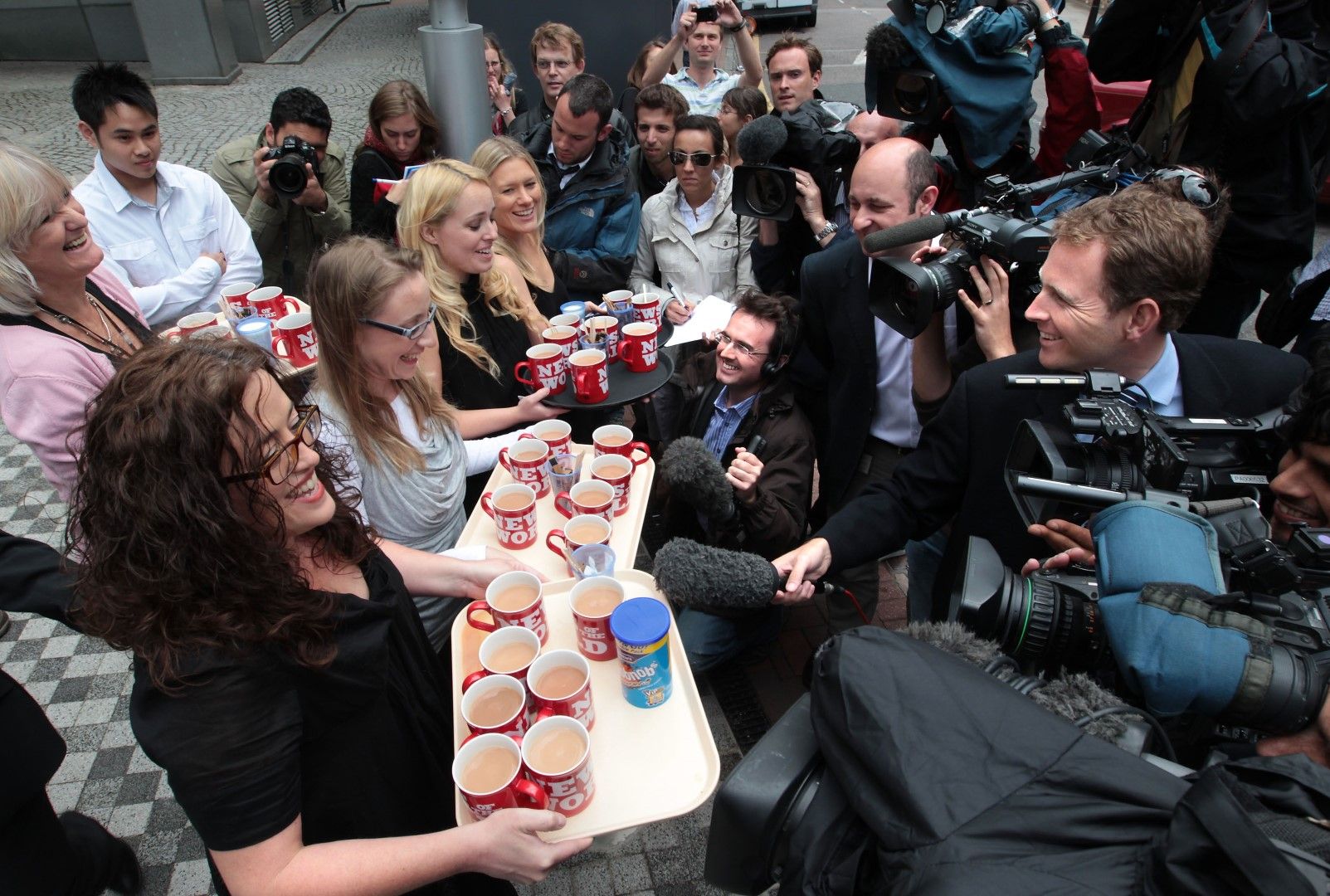 Служители на News of The World (от ляво) Хелън Мос, Франсин Пакър, Хана Ийдс и Джейн Хамилтън поднасят брандирани с логото на закрития вестник чаши чай на чакащите репортери пред офиса на News International на 9 юли 2011 г. 