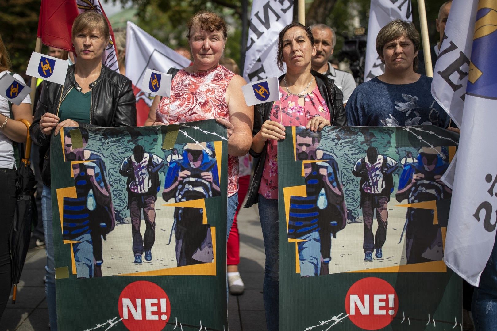 Протестиращи държат плакати с надпис „Не на бежански лагер в малкия град Девенискес“ по време на антимигрантски протест пред правителствения дворец във Вилнюс, Литва, 29 юли