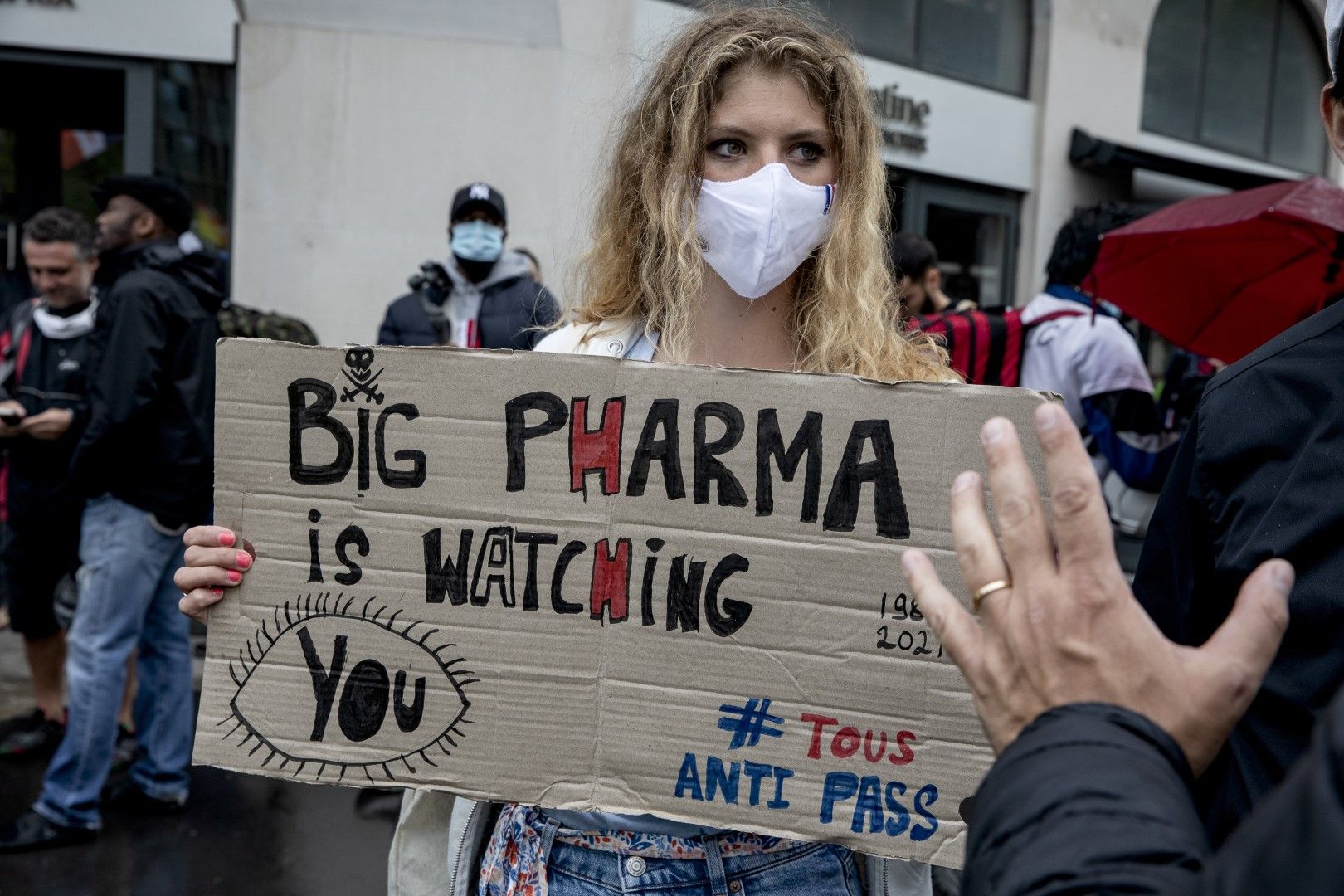 Жена държи направен от картон плакат, на който пише „Голямата фармация ви наблюдава“ по време на протест срещу ваксините и ваксинационните паспортите в Париж, Франция, събота, 7 август 2021 г.