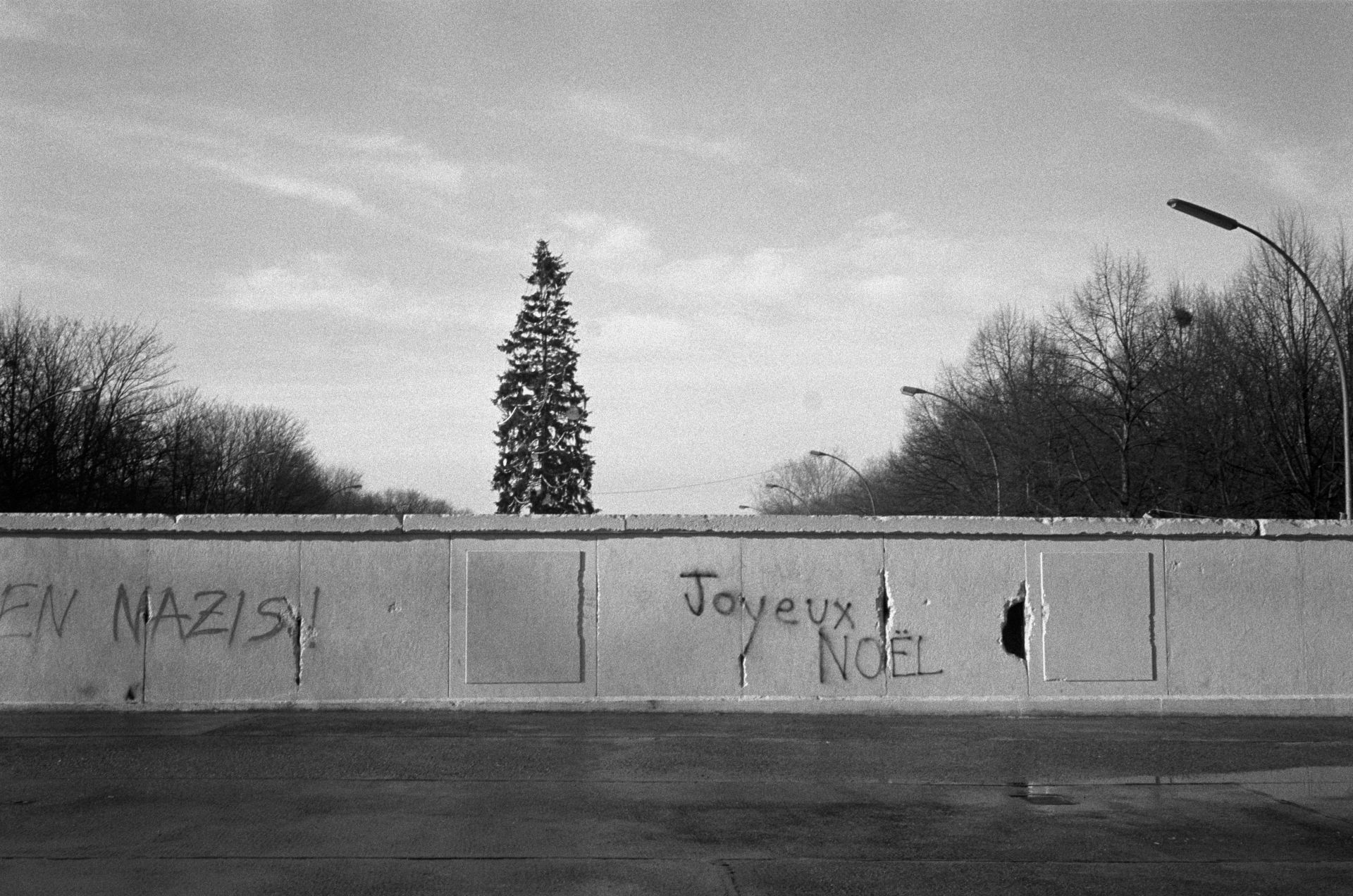 Първите графити по Берлинската стена се появяват още в годината на събарянето ѝ - 1989 г.  На снимката се вижда украсена Коледна елха от западната страна на стената