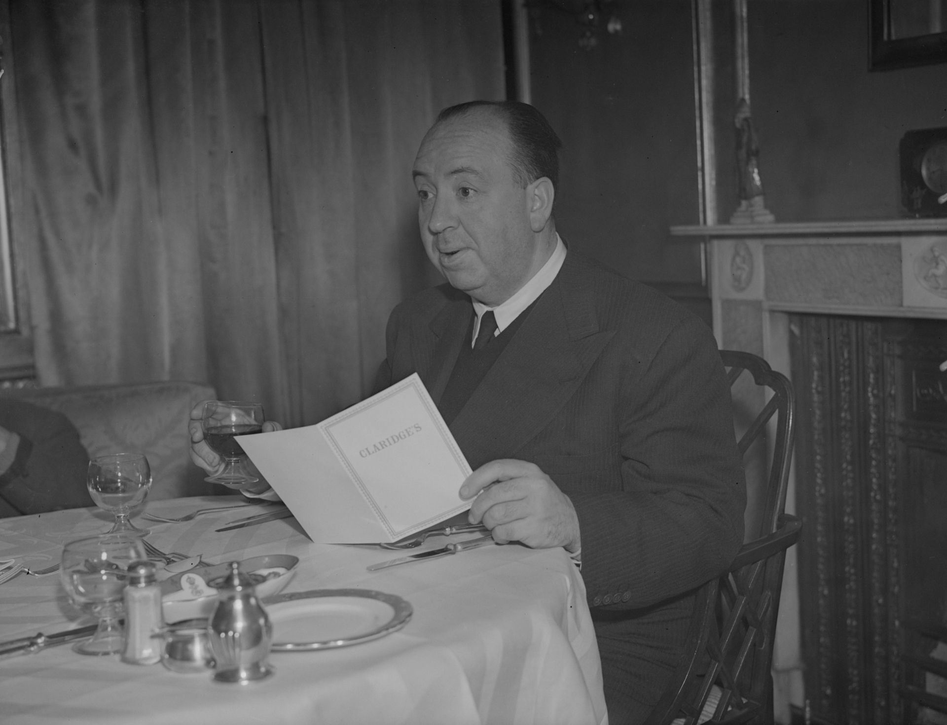 Алфред Хичкок пийва чаша вино, докато си избира ястие от менюто през 1943 г. в Лондон