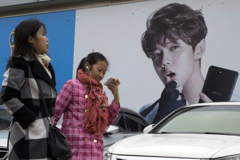 Китайки минават покрай реклама с тийнейджърския идол Лу Хан, известен също като китайския Джъстин Бийбър, в Пекин