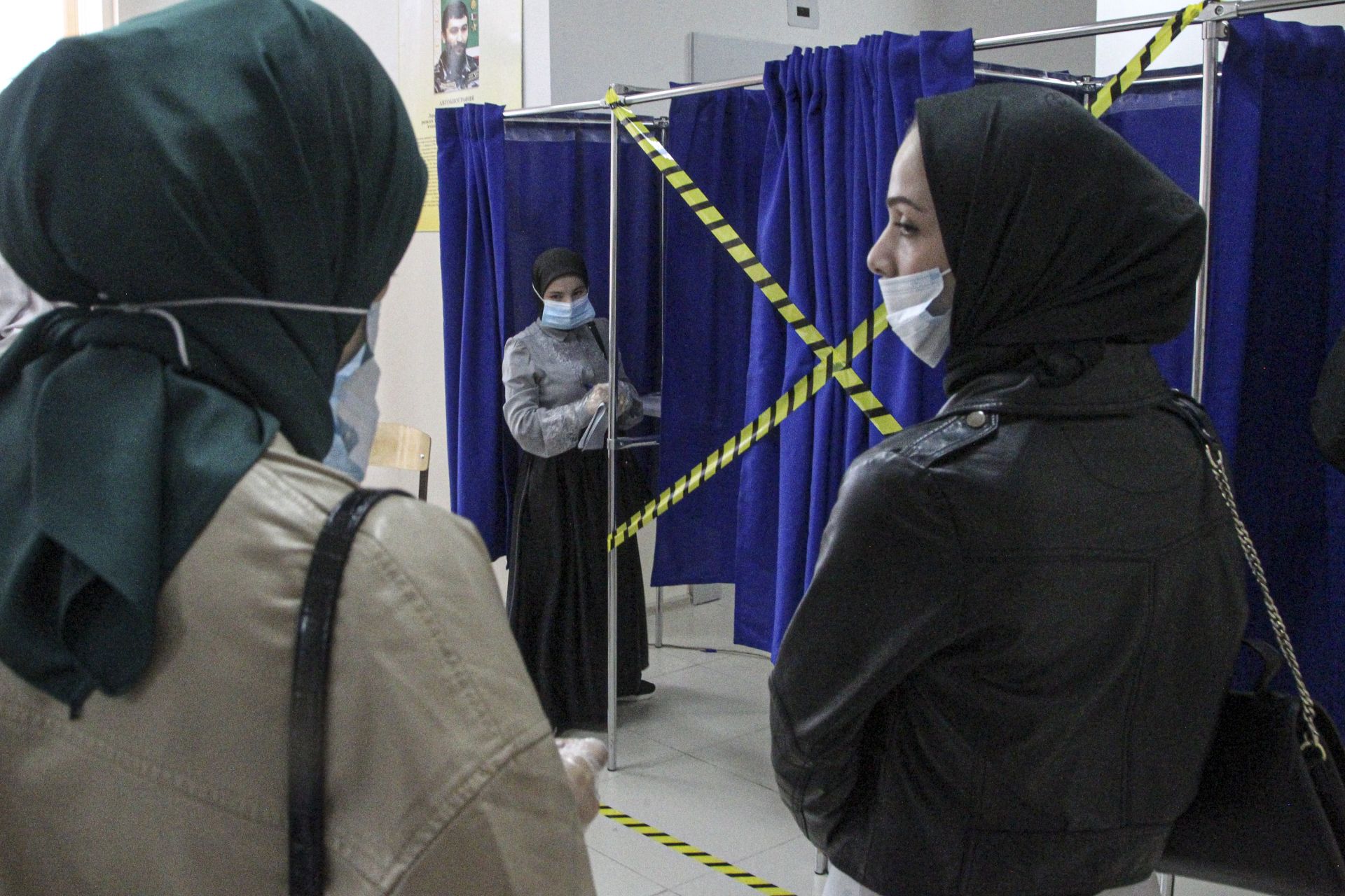 Чеченските жени чакат да попълнят бюлетините си в кабината за гласуване на избирателна секция по време на парламентарните избори в Грозни