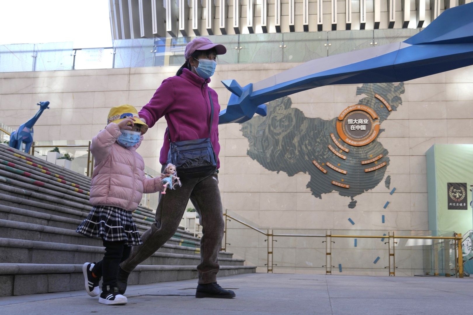 Жители, носещи маски, минават покрай рекламно пано, изобразяващо операциите на Evergrande Group в Китай в един от техните търговски проекти в Пекин