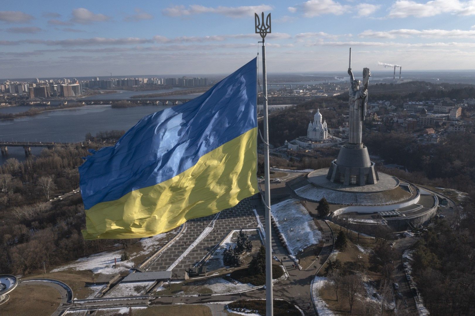 Изглед към националния флаг на Украйна, който се развява над столицата Киев с паметника на Родината вдясно, неделя, 13 февруари 2022 г.