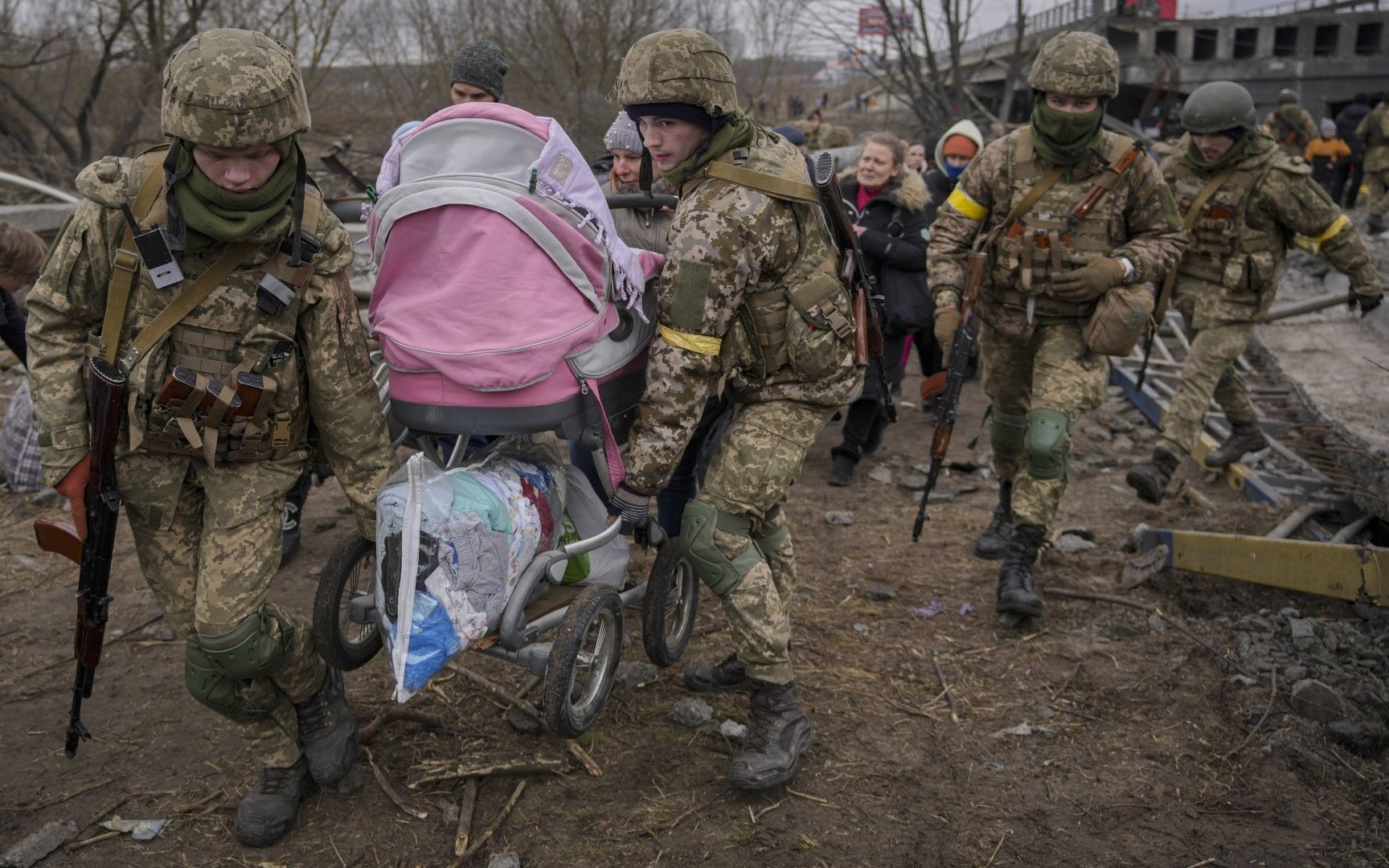 Украински военнослужещи носят бебешка количка, след като прекосиха река Ирпин по импровизирана пътека под мост, който беше разрушен от руски въздушен удар, 5 март