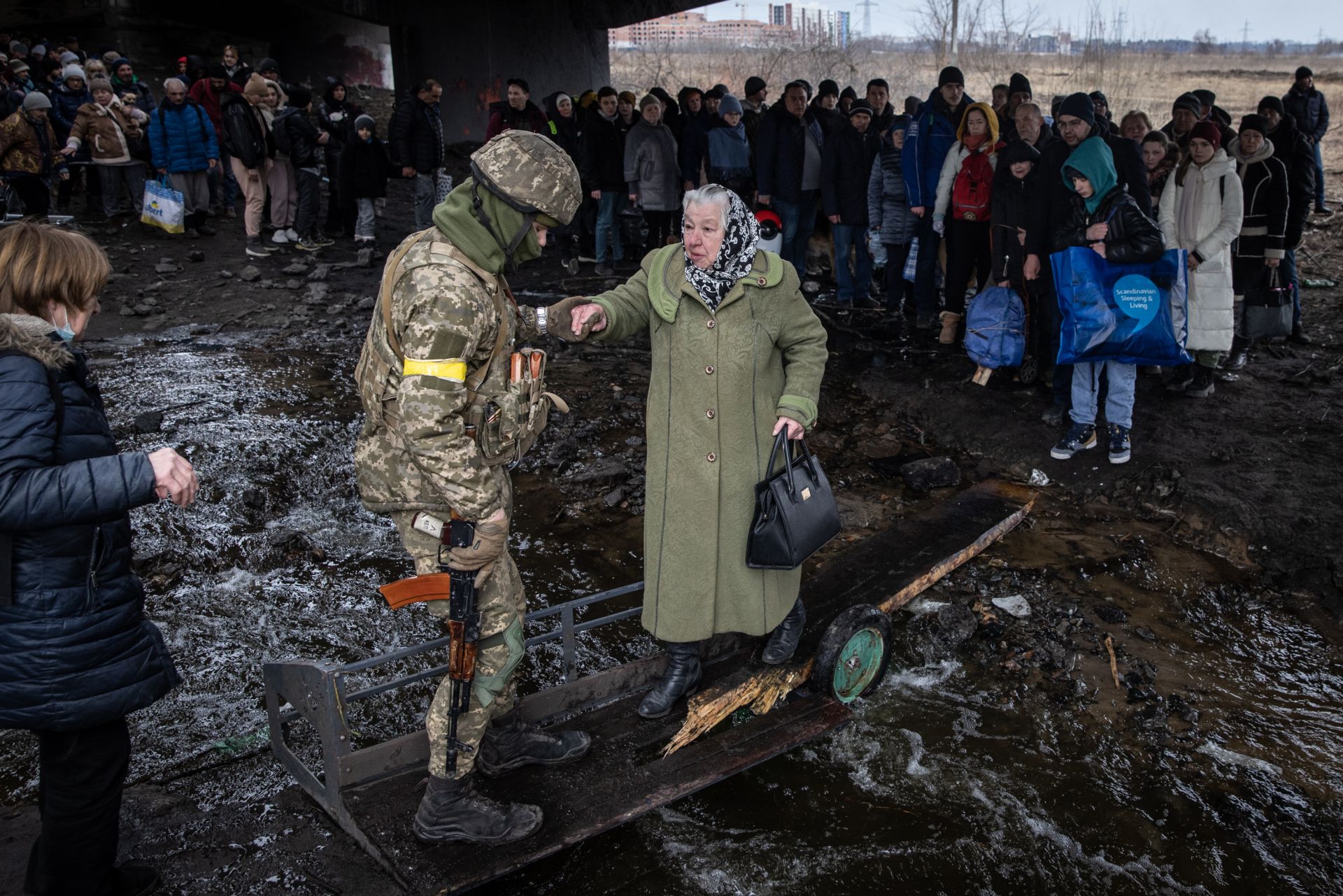Войник помага на жена да премине през рарушения мост в Ирпен 