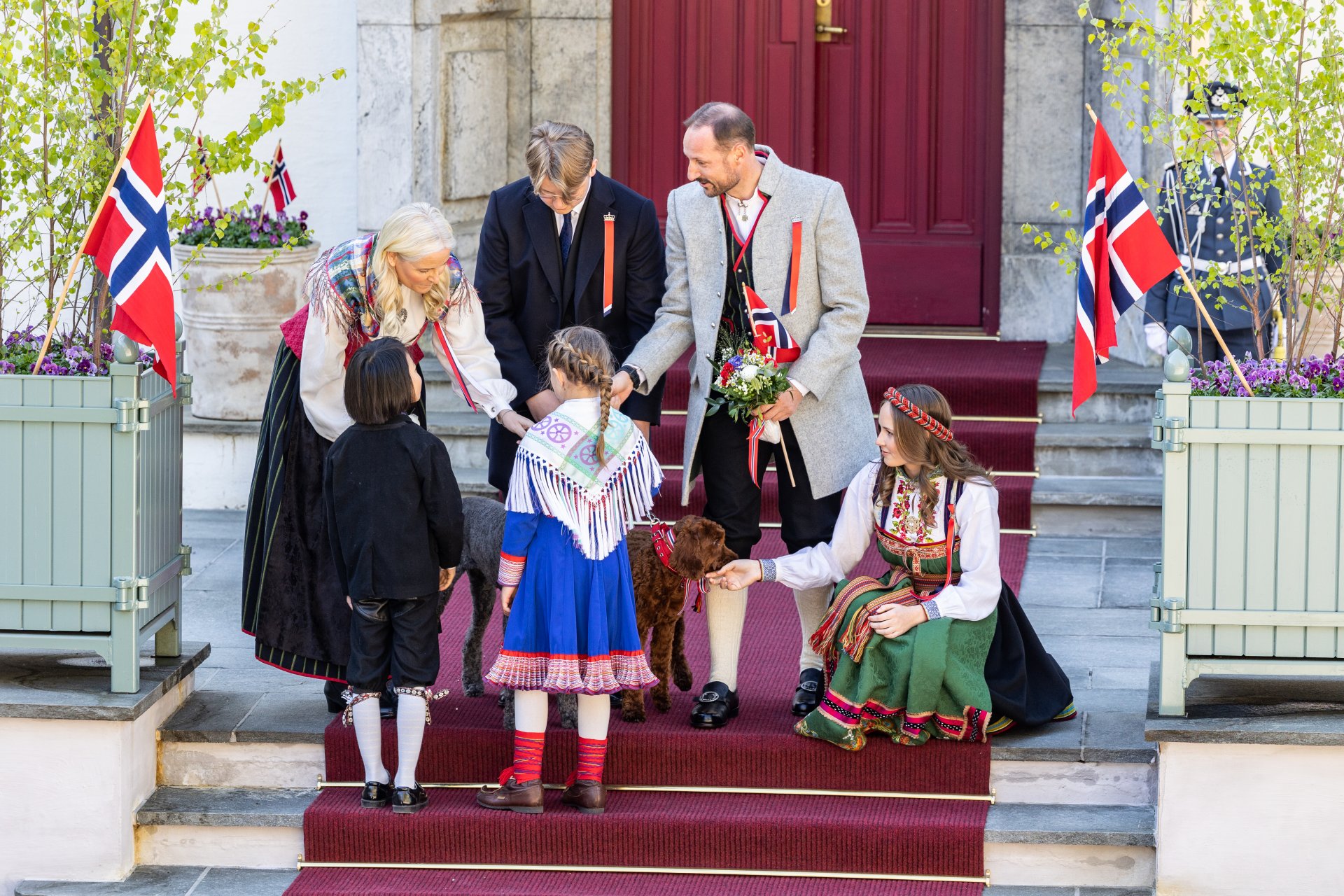 Престолонаследникът Мете-Марит от Норвегия, принц Свере Магнус от Норвегия, престолонаследникът Хокон от Норвегия и принцеса Ингрид Александра от Норвегия получават цветя от две деца по време на детския парад в Скаугум, Аскер на Норвегия, който е  Национален празник (отляво надясно).
