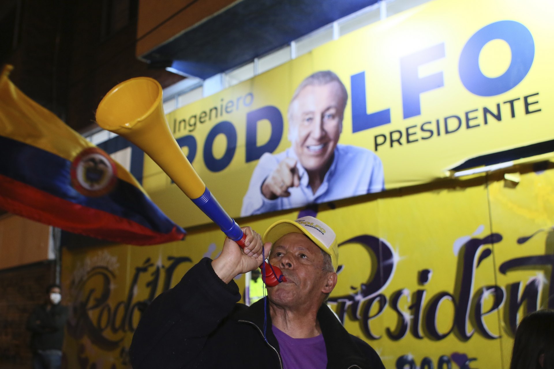 Привърженик на Родолфо Ернандес, кандидат за президент надува рог пред надписите на кампанията на кандидата в изборната нощ в Богота